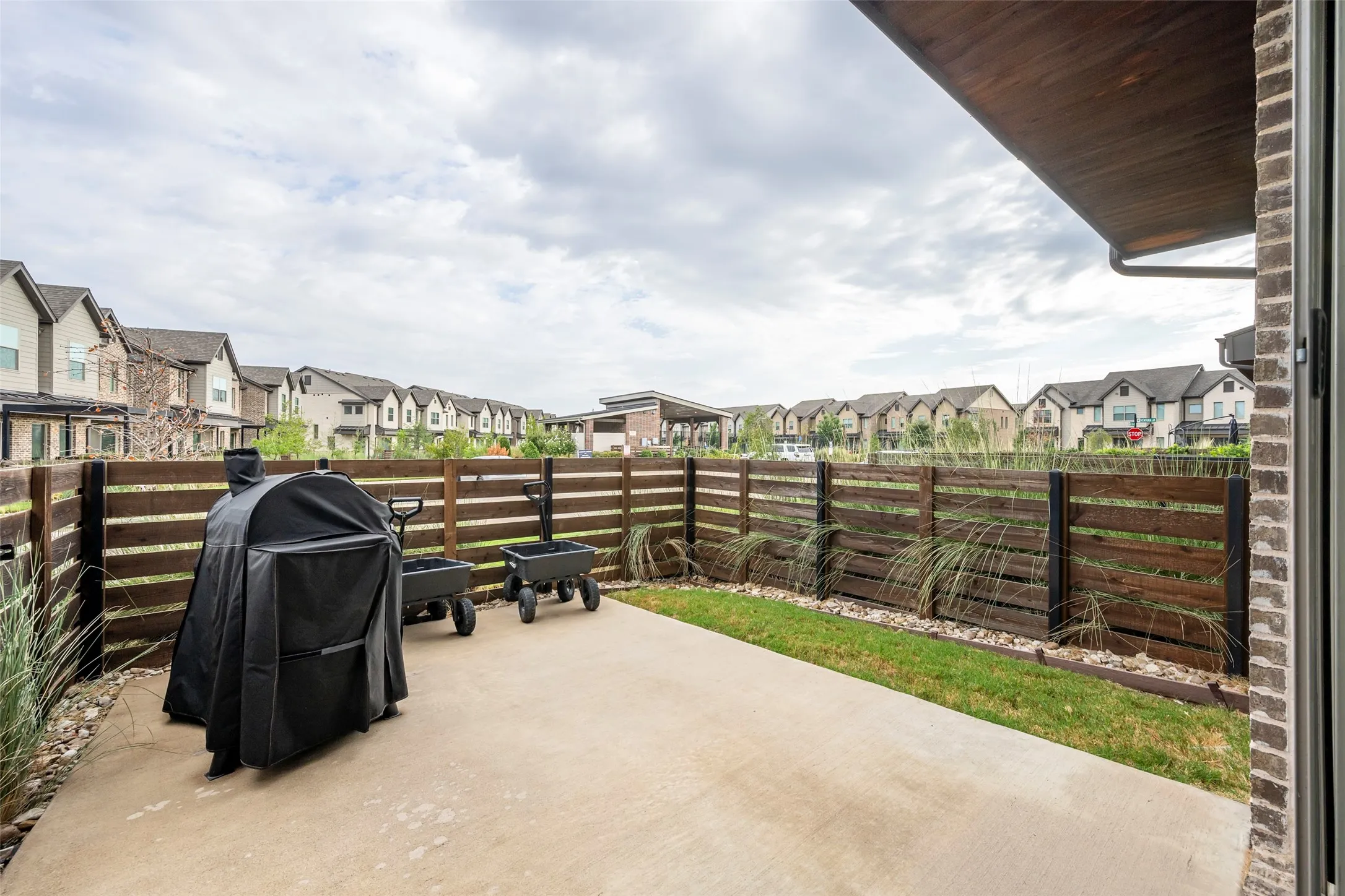 Concrete patio with wood-finish horizontal privacy fence, low-maintenance landscaping, and brick exterior detail