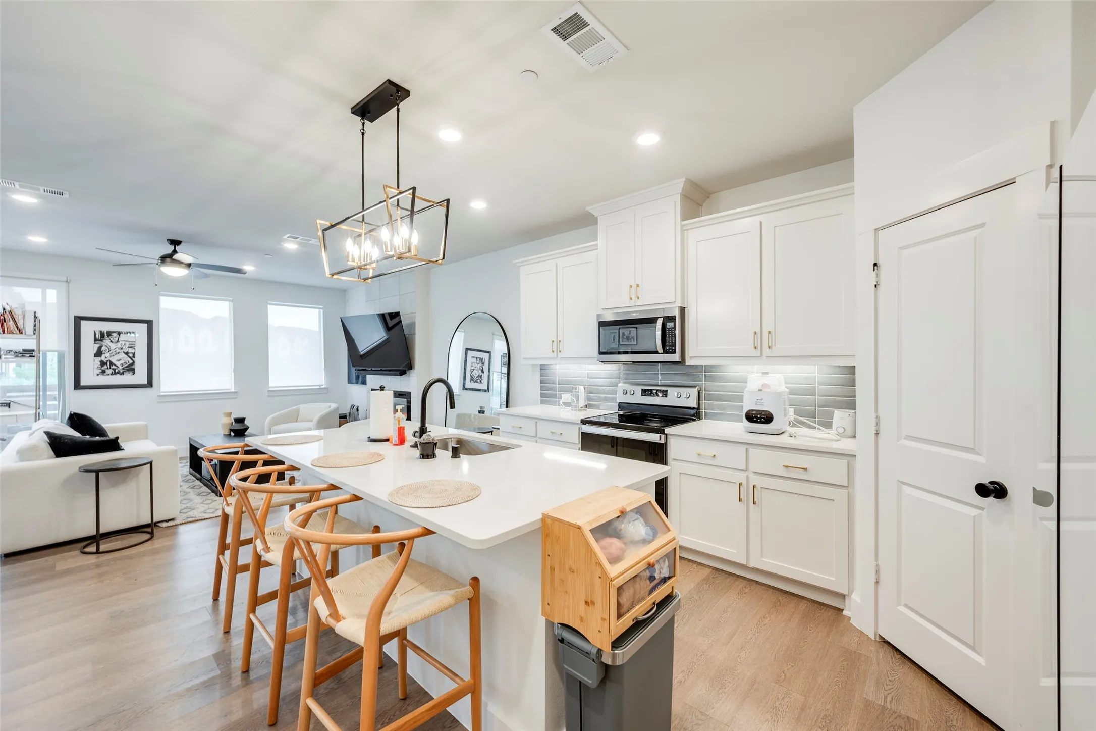 Open-concept living space featuring wood-finish flooring, a kitchen island with seating, white cabinetry, integrated microwave, and a tile backsplash