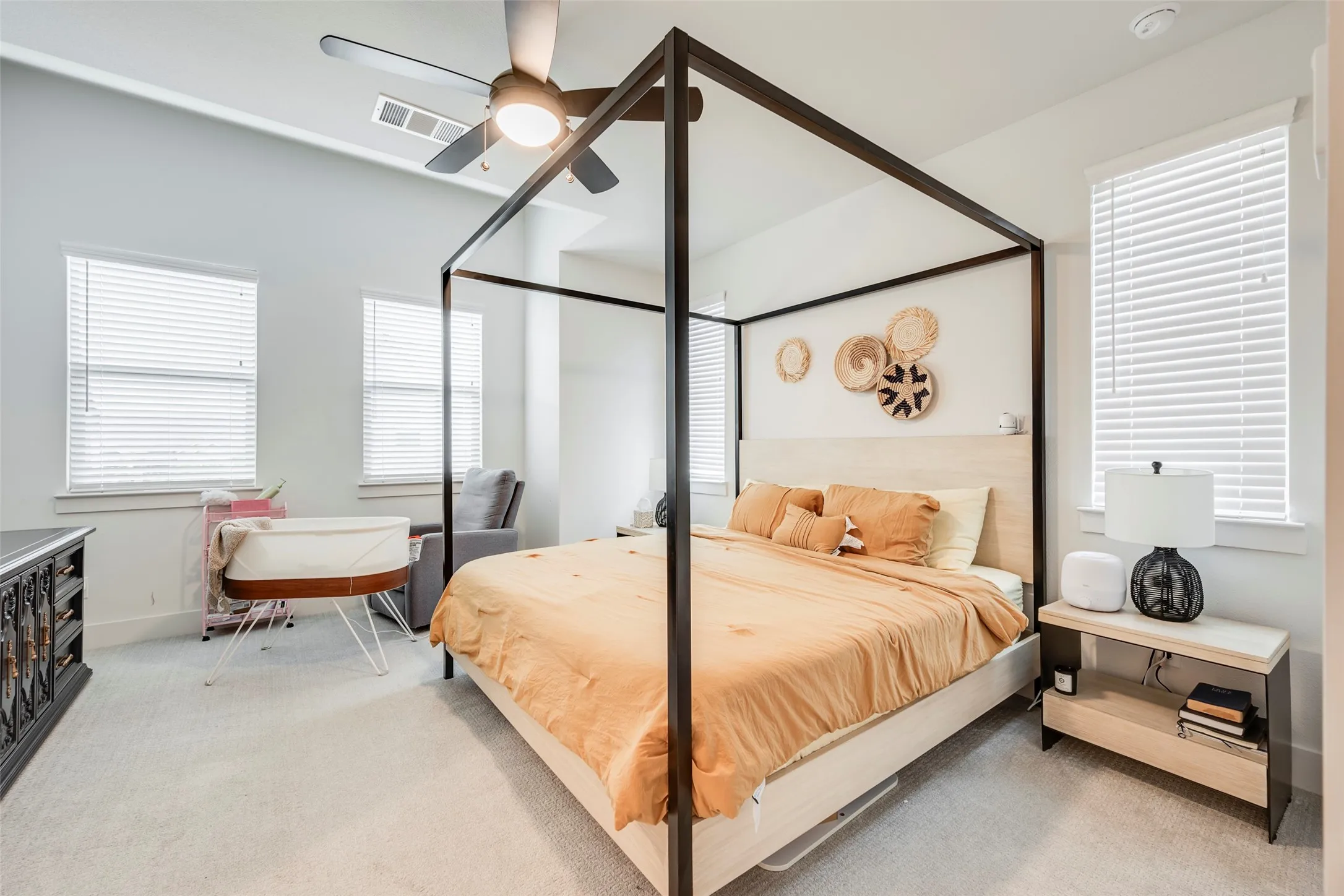 Light-colored carpeting, two large windows with blinds, and a ceiling fan with integrated lighting