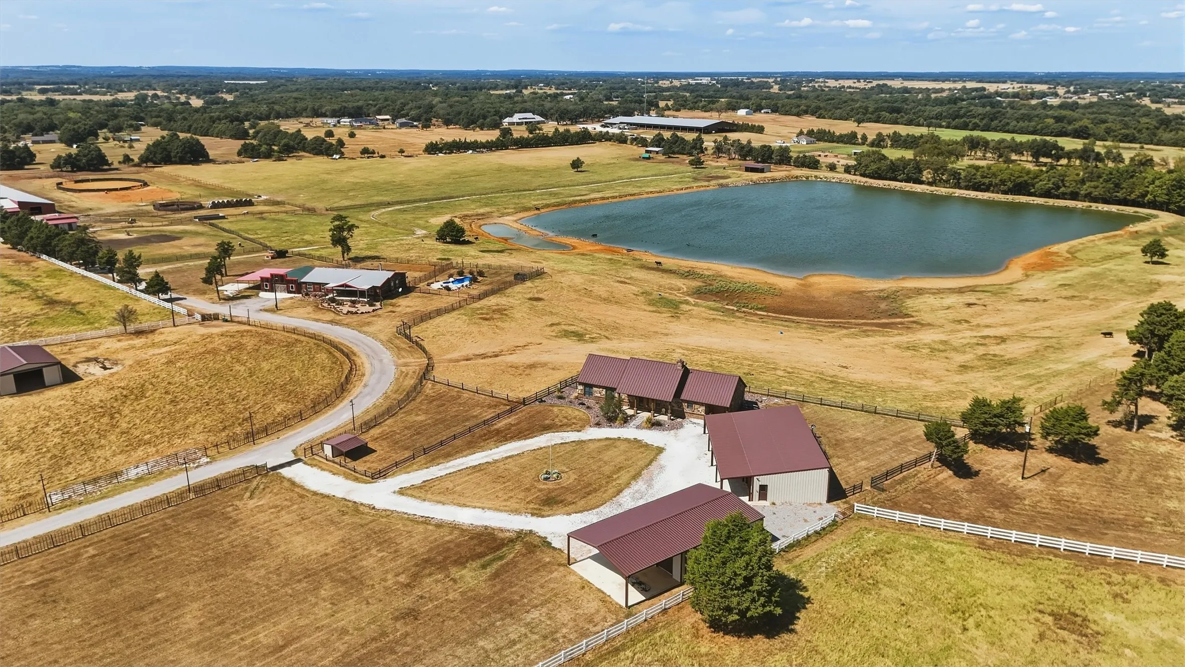 Aerial view showing circular drive and custom home and outbuildings with equine facilities to the east.