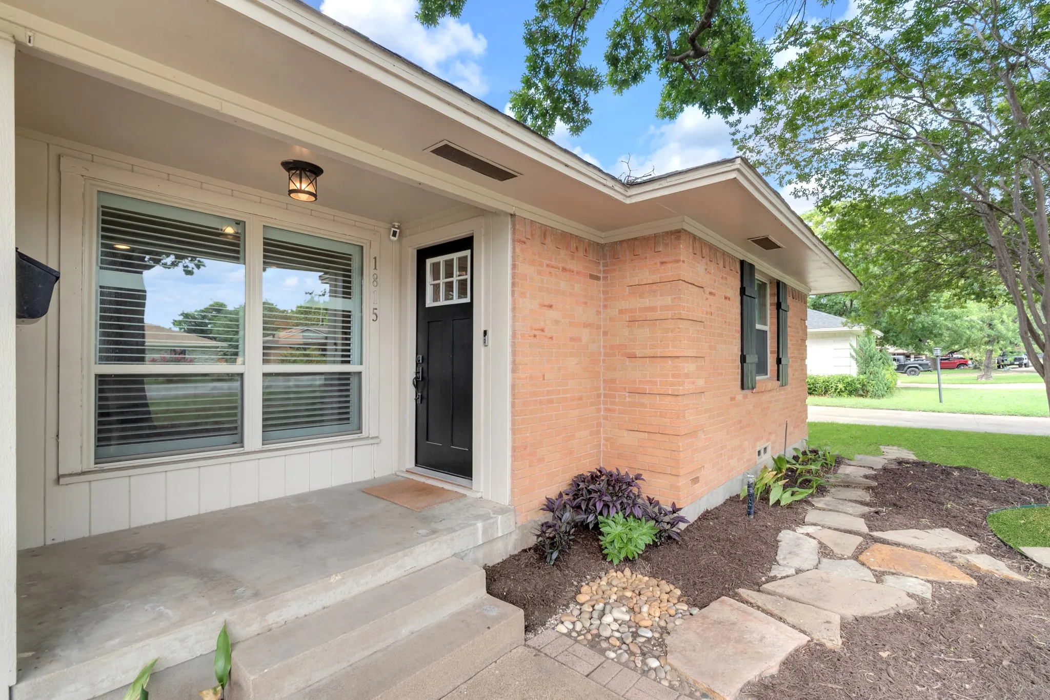 Brick exterior featuring a black front door with decorative window inserts, an overhead porch light, and an adjacent multi-pane window