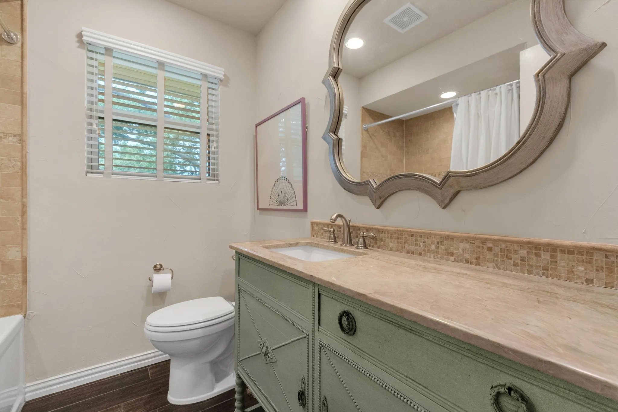 Bathroom featuring a vanity with an integrated sink, a large decorative mirror, and a window with horizontal blinds