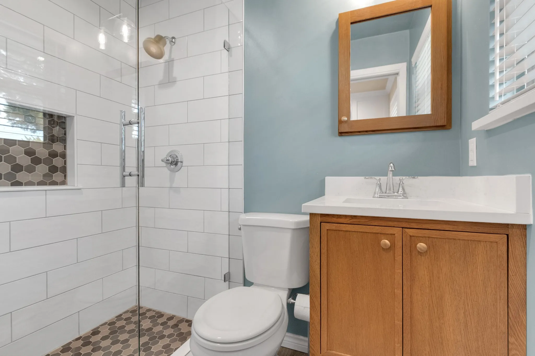 Bathroom featuring a glass-enclosed shower with white subway tile, hexagonal mosaic floor tiling, and a built-in shower niche