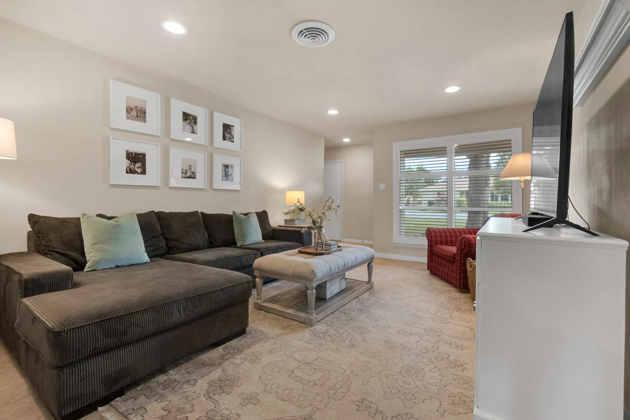 Spacious living area featuring neutral wall tones, recessed lighting, and a large window with horizontal blinds