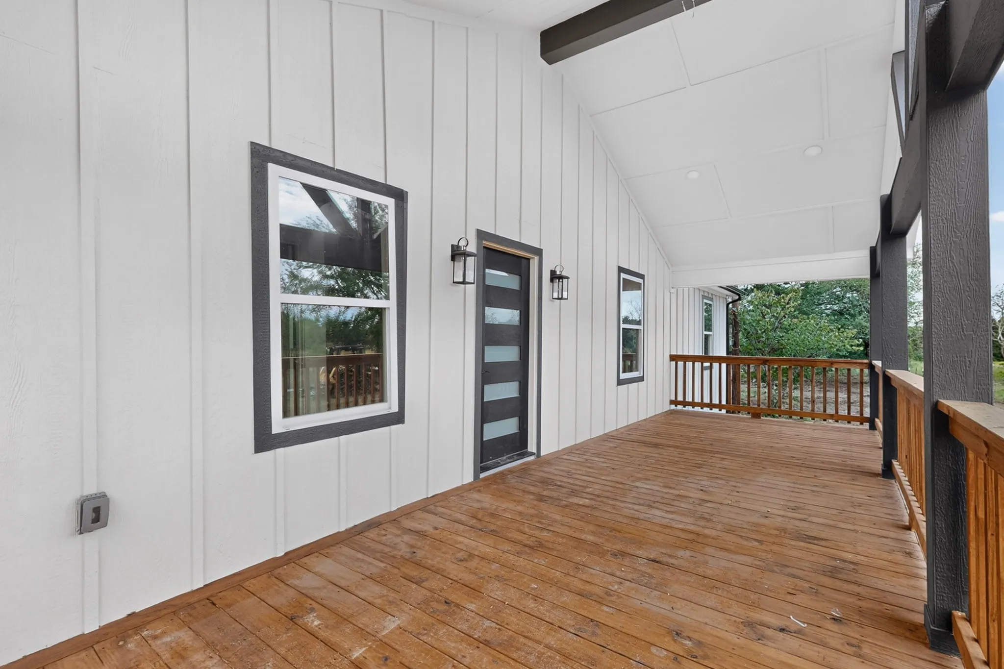 Expansive covered porch featuring wood-finish decking, white board-and-batten siding, and dark-framed windows