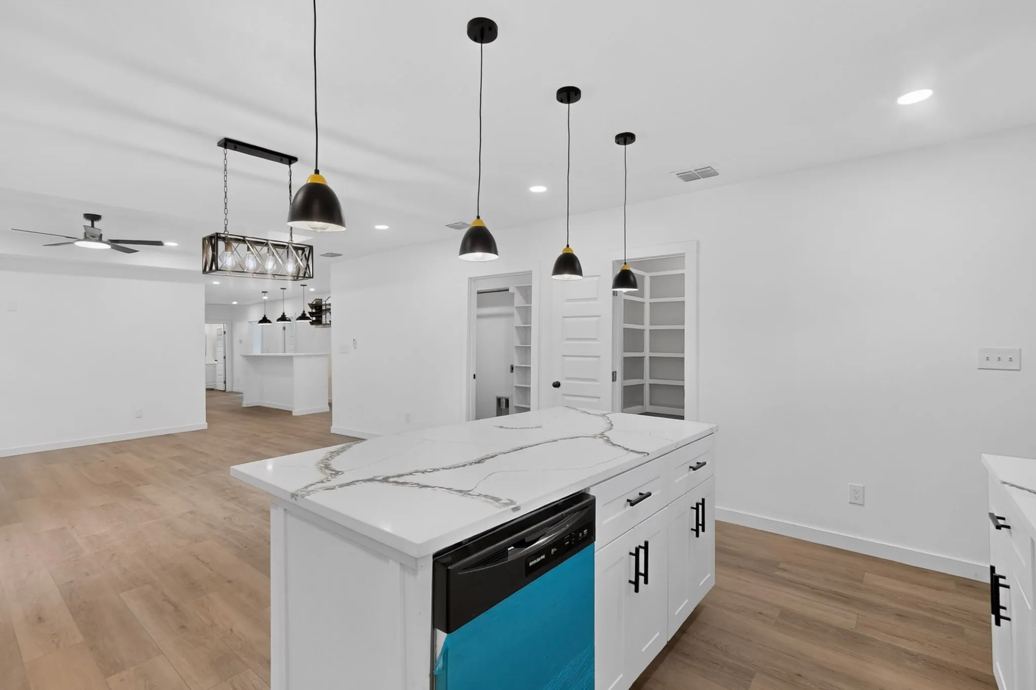 Kitchen island with a white countertop featuring black veining, dark pendant lighting, and wood-finish flooring