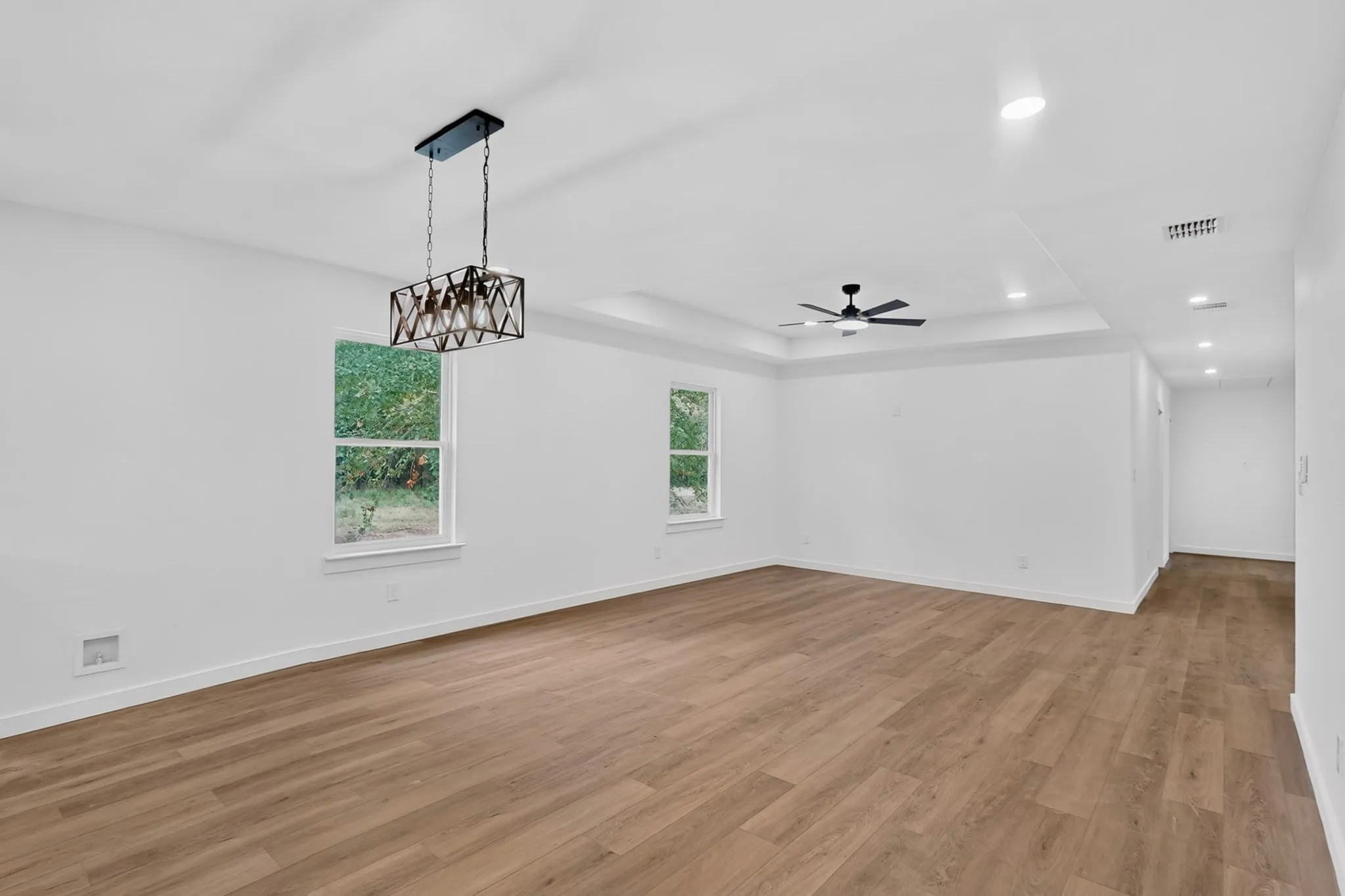 Wood-finish flooring, recessed lighting, ceiling fan, decorative chandelier, and tray ceiling