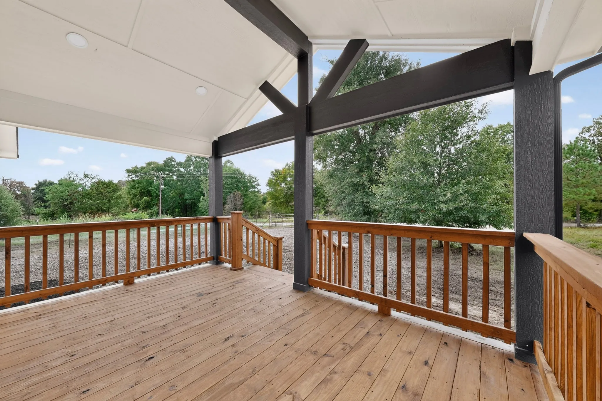 Expansive covered deck featuring natural wood flooring and railings, a vaulted ceiling with recessed lighting, and exposed structural beams