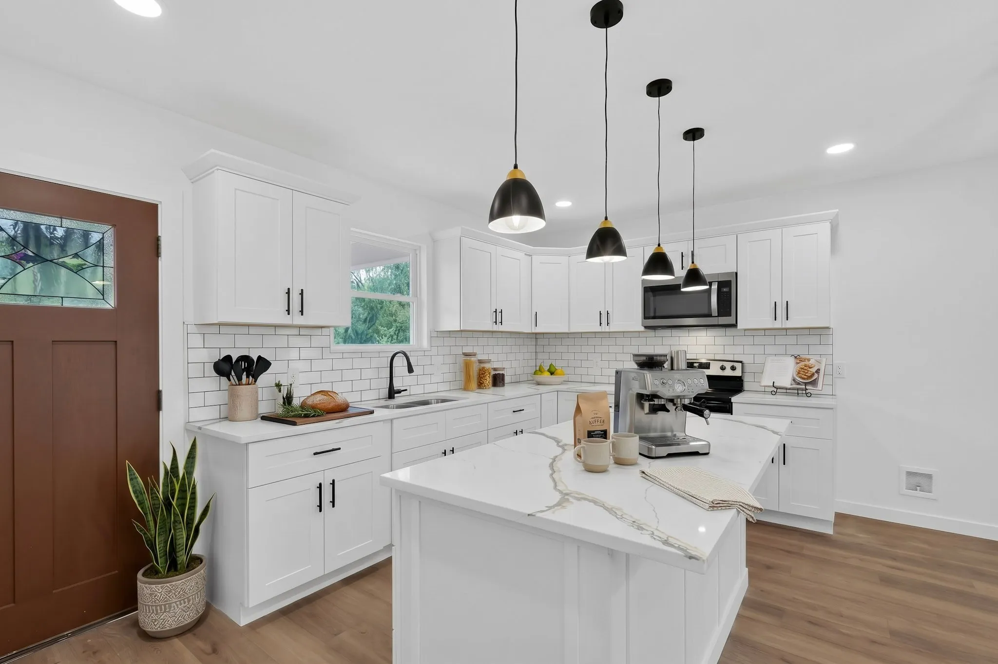 White shaker-style cabinetry with black hardware, subway tile backsplash, white quartz countertops, wood-finish flooring, and pendant lighting