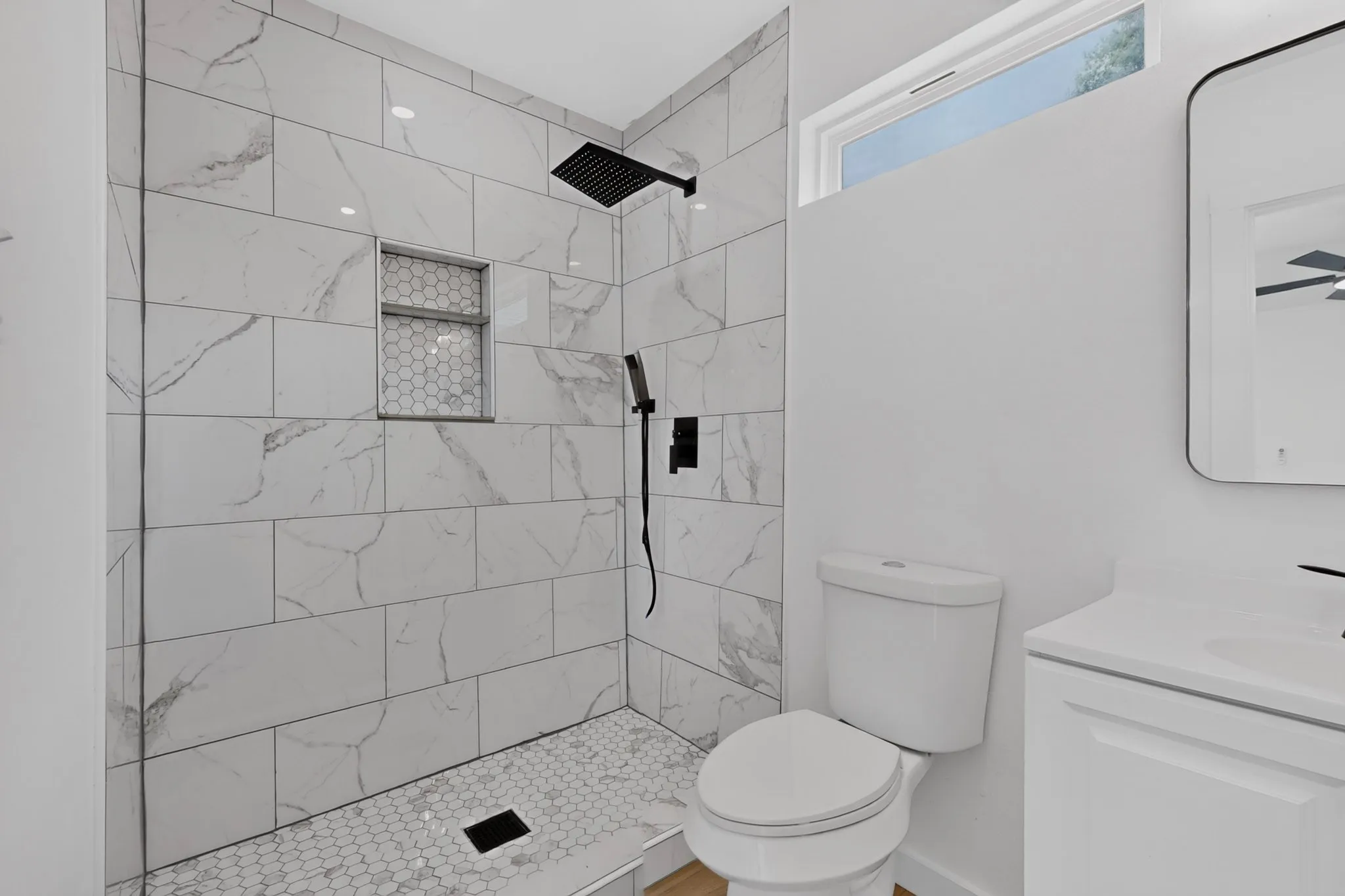 Tiled shower with a rain showerhead, recessed niche with hexagonal tile, and hexagonal tile flooring