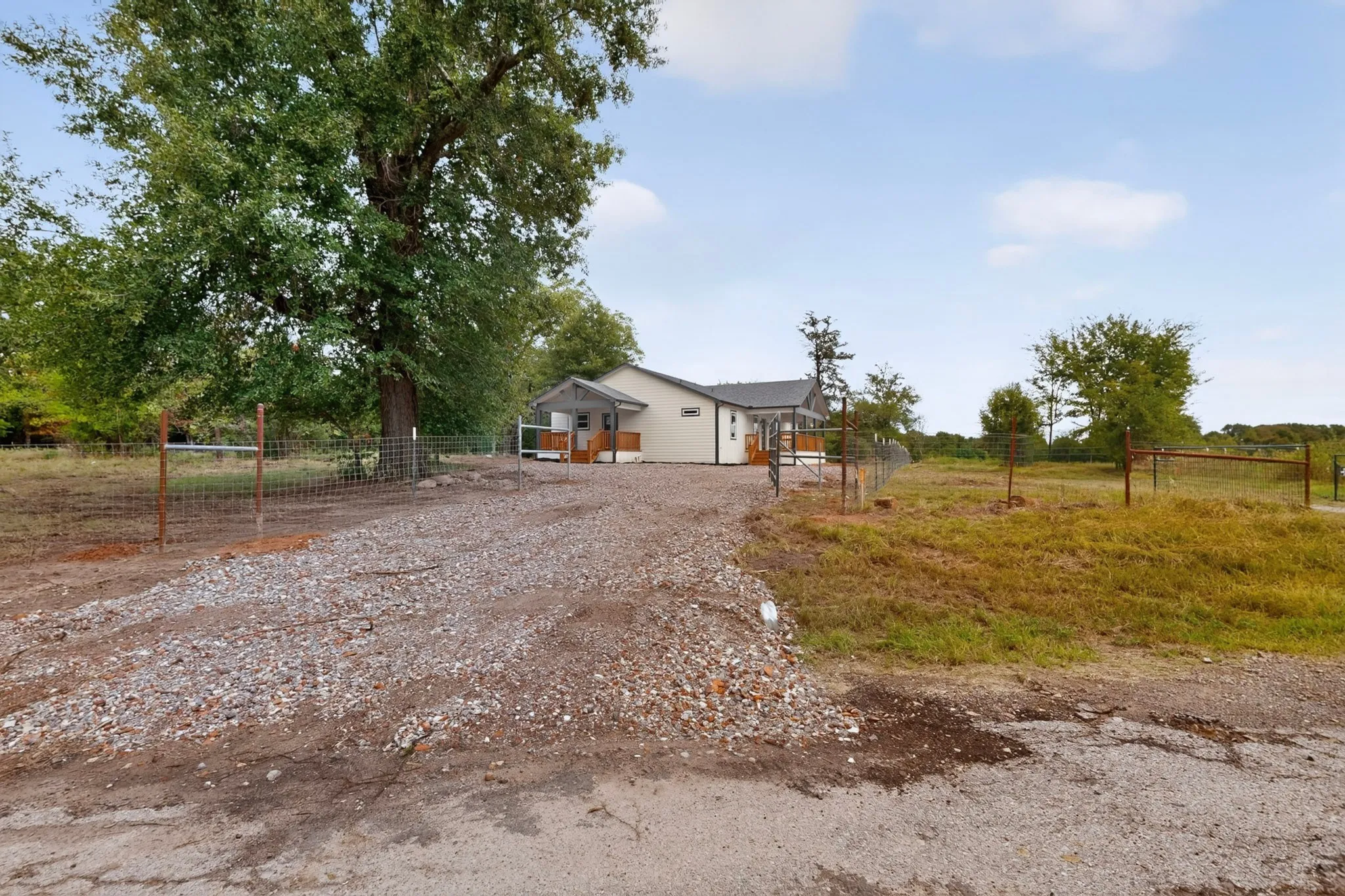 Gravel driveway leading to a residence with a covered porch and fenced perimeter