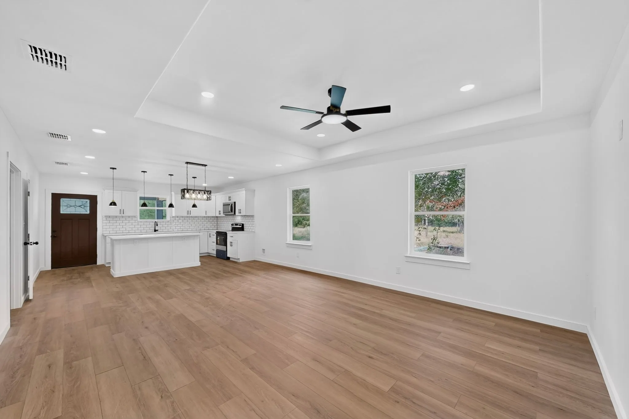 Open-concept living space with wood-finish flooring, recessed lighting, and a tray ceiling