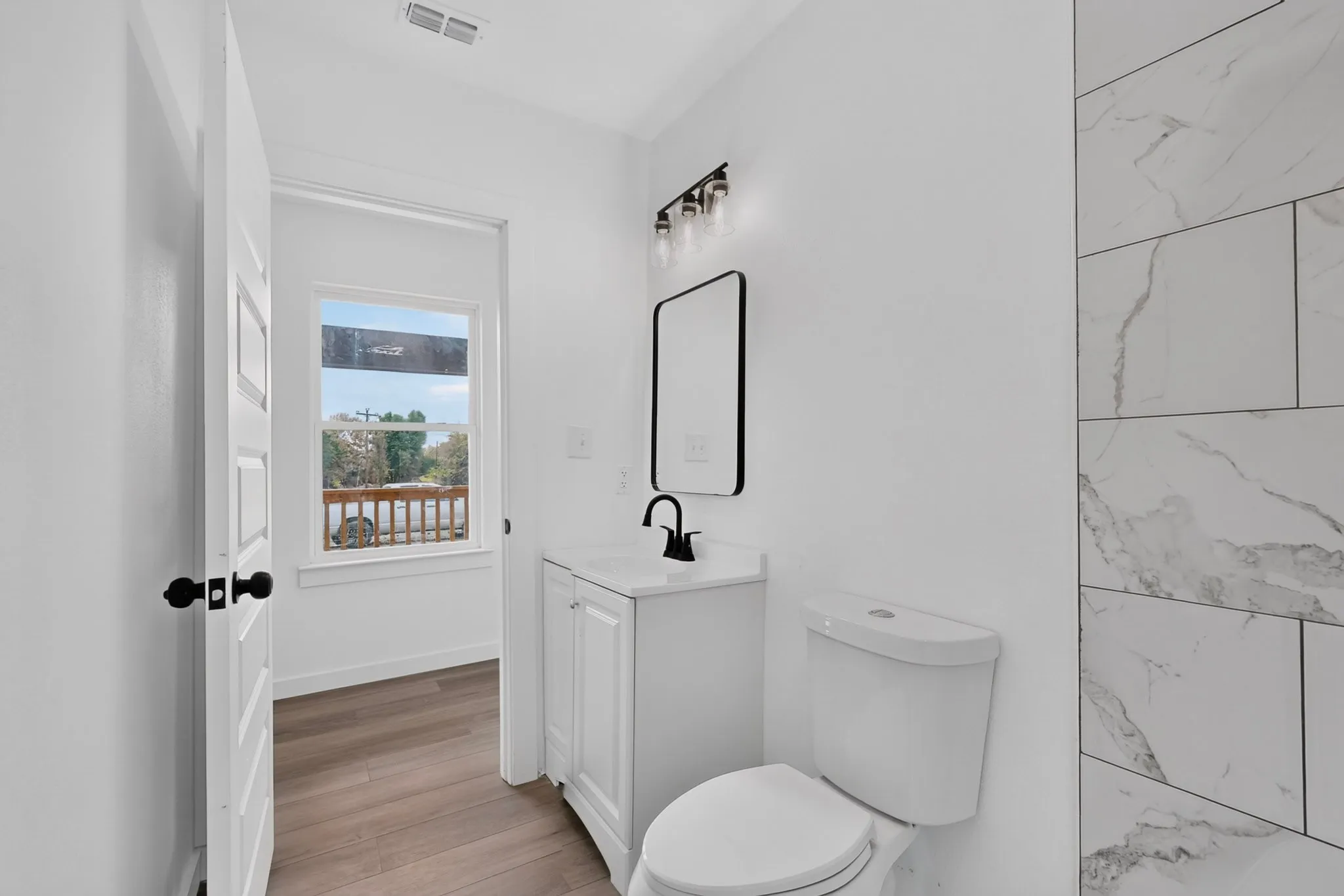 White vanity with integrated sink, matte black faucet, rectangular framed mirror, and vertical format wall tiling with a natural stone pattern