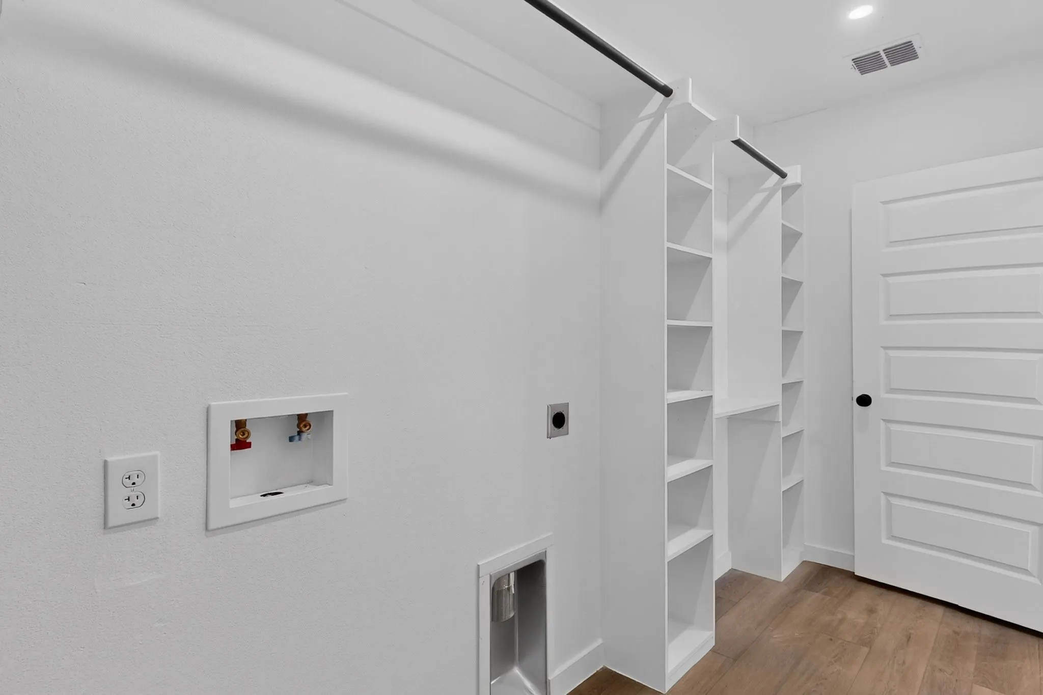 Laundry area featuring built-in shelving, hanging rods, wood-finish flooring, and a panel door