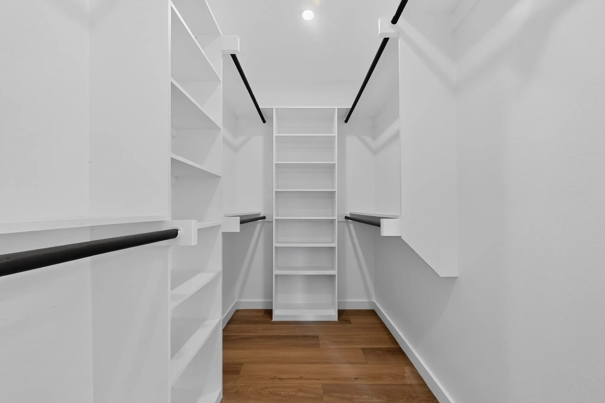 Walk-in closet with extensive built-in shelving, multiple hanging rods, recessed lighting, and wood-finish flooring