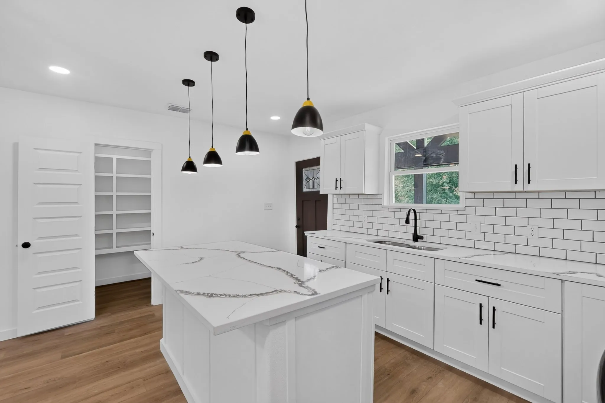 Kitchen featuring white shaker cabinetry, patterned stone countertops, a subway tile backsplash, and a large pantry with built-in shelving