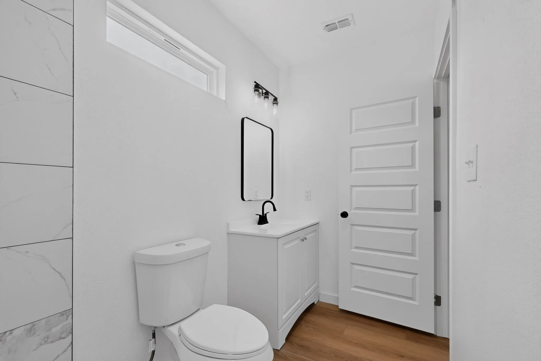 White vanity with integrated sink and matte black faucet, wall-mounted mirror, modern panel interior door, and wood-finish flooring