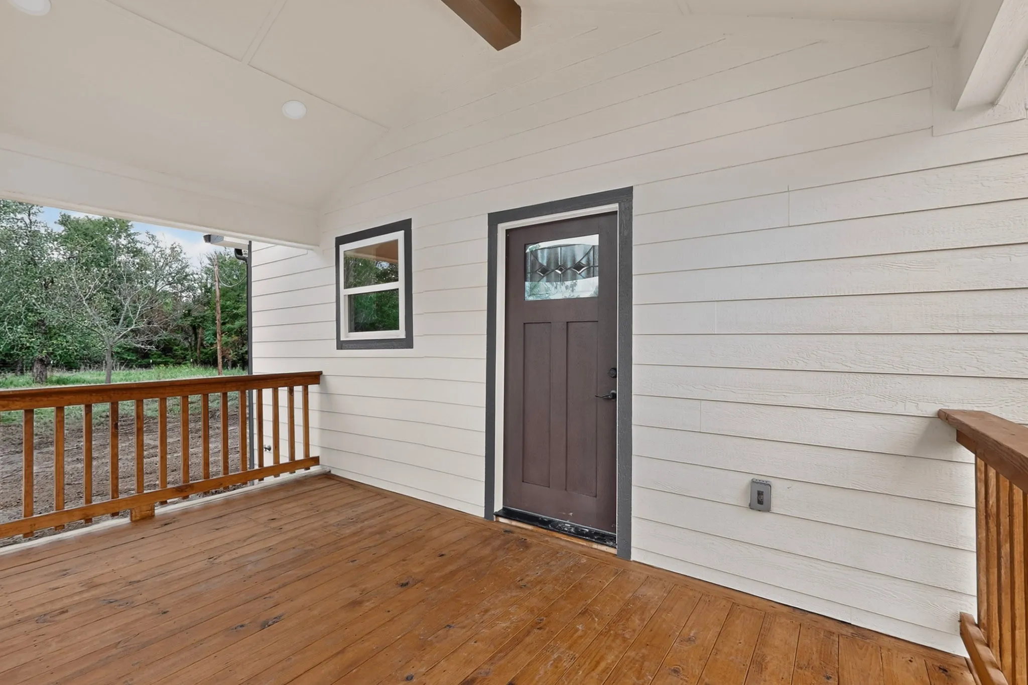 Covered porch featuring wood-finish decking, painted wood siding, and a paneled entry door with decorative glass