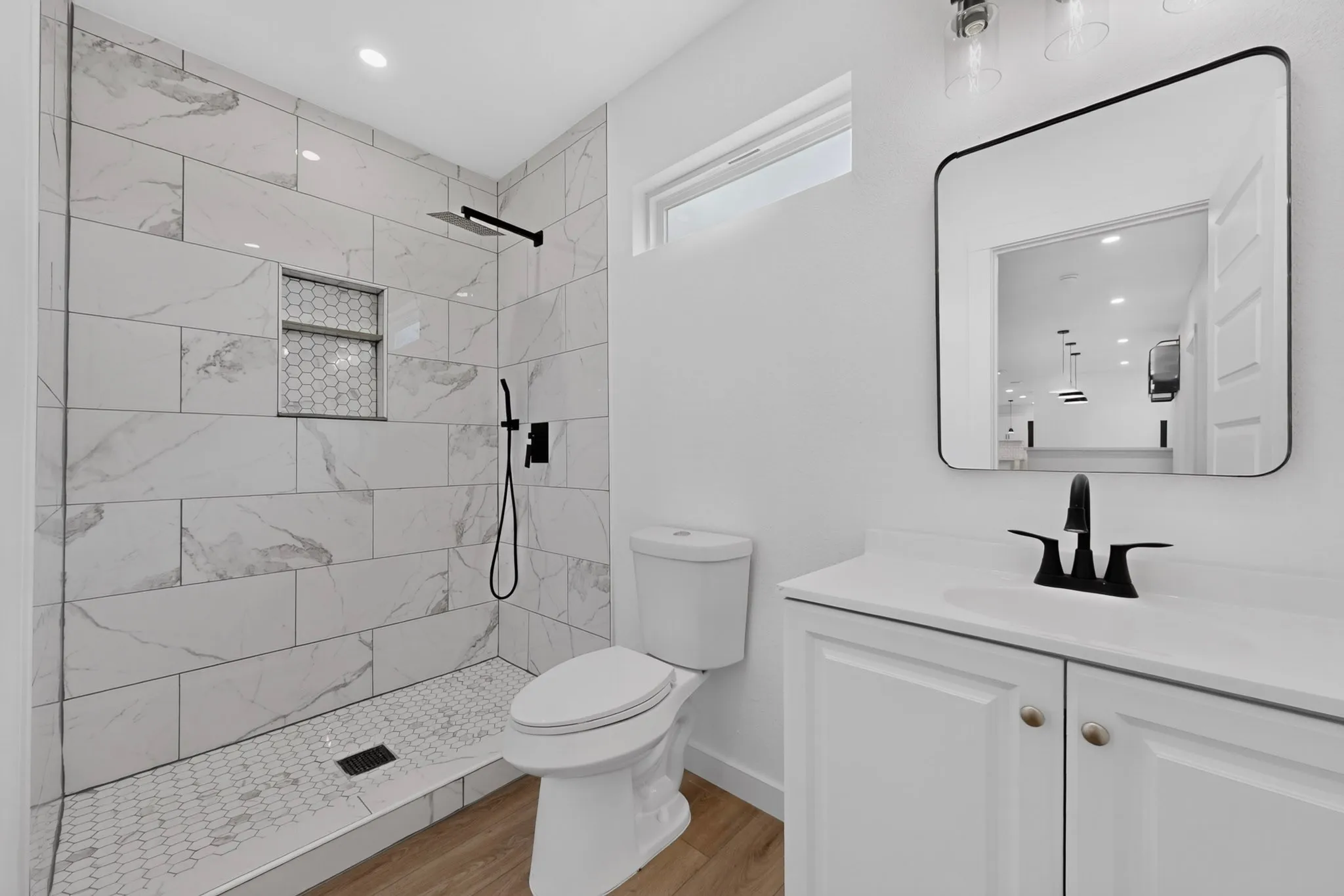Modern bathroom featuring a walk-in shower with large format wall tiles and a hexagonal floor, a built-in shower niche, a white vanity with a rectangular sink, and a black-framed mirror