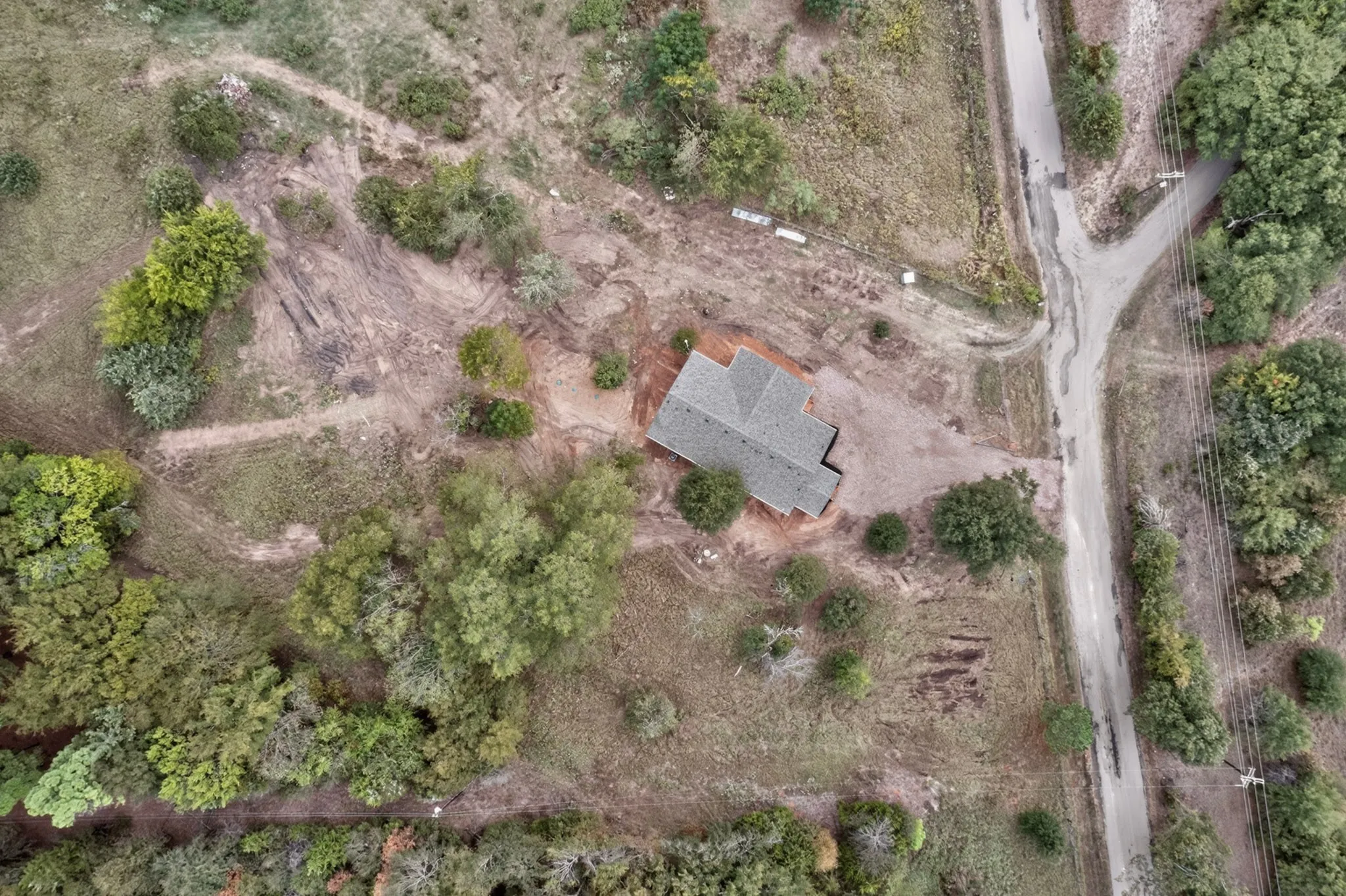 Property featuring a gabled roofline, surrounding mature trees, and an unpaved road