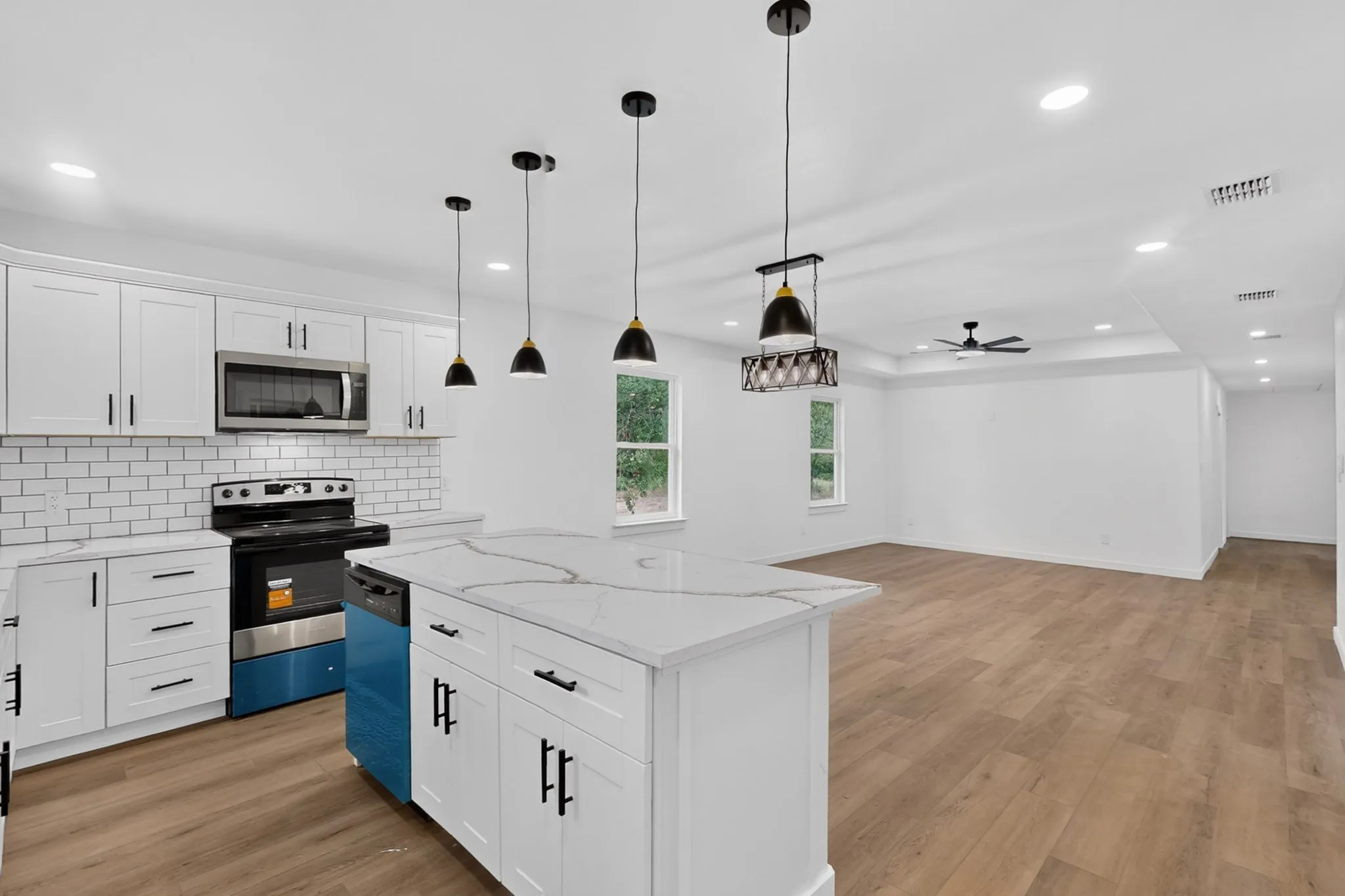 White shaker cabinetry with matte black hardware, stainless steel appliances, a subway tile backsplash, a kitchen island with a light-toned countertop, and wood-finish flooring