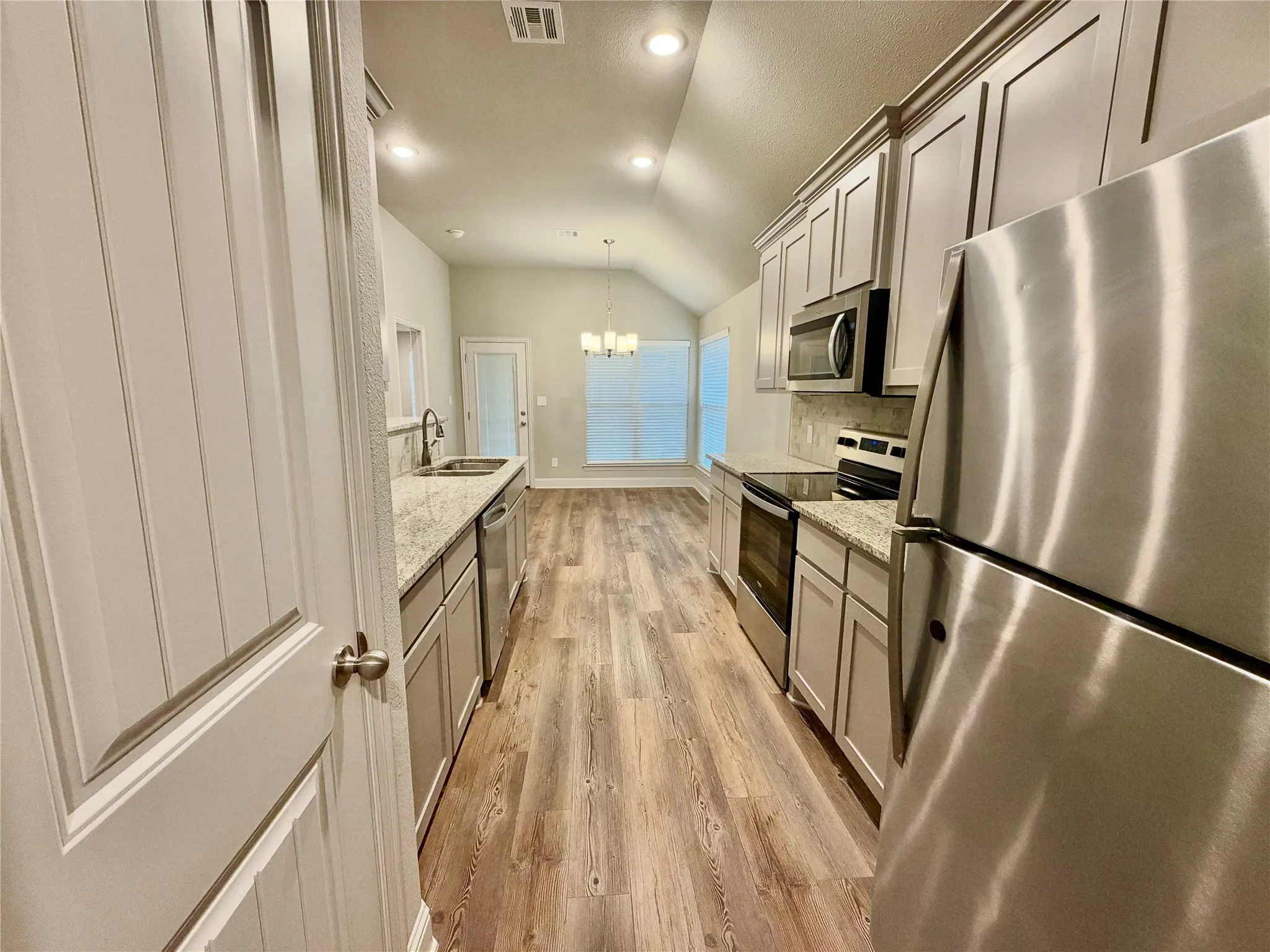 Kitchen featuring stainless steel appliances, wood-finish flooring, light-toned cabinetry, granite countertops, and recessed lighting