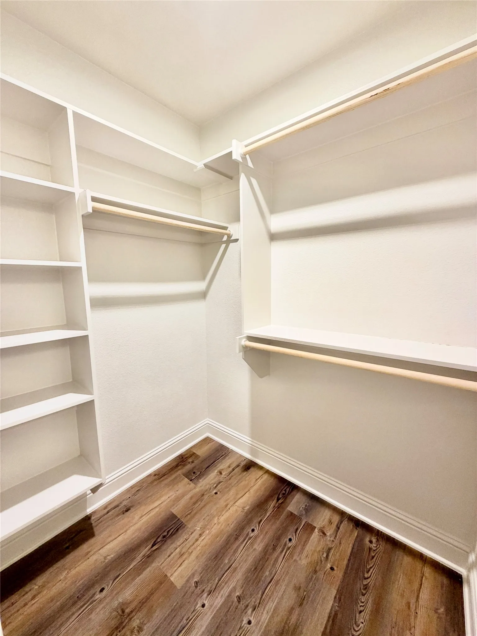Custom closet system with built-in shelving, multiple hanging rods, and wood-finish flooring