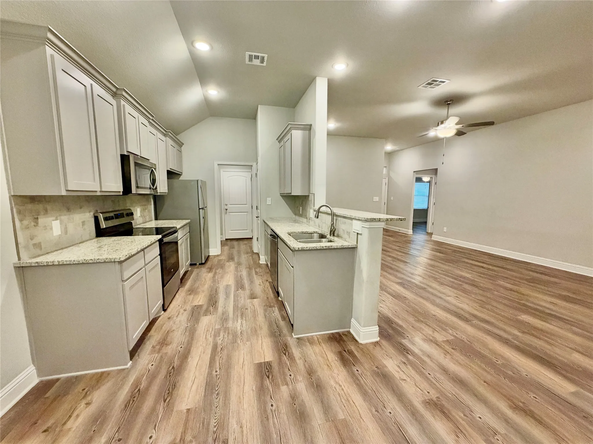Open-concept kitchen featuring wood-finish flooring, light-toned cabinetry, stainless steel appliances, and a breakfast bar