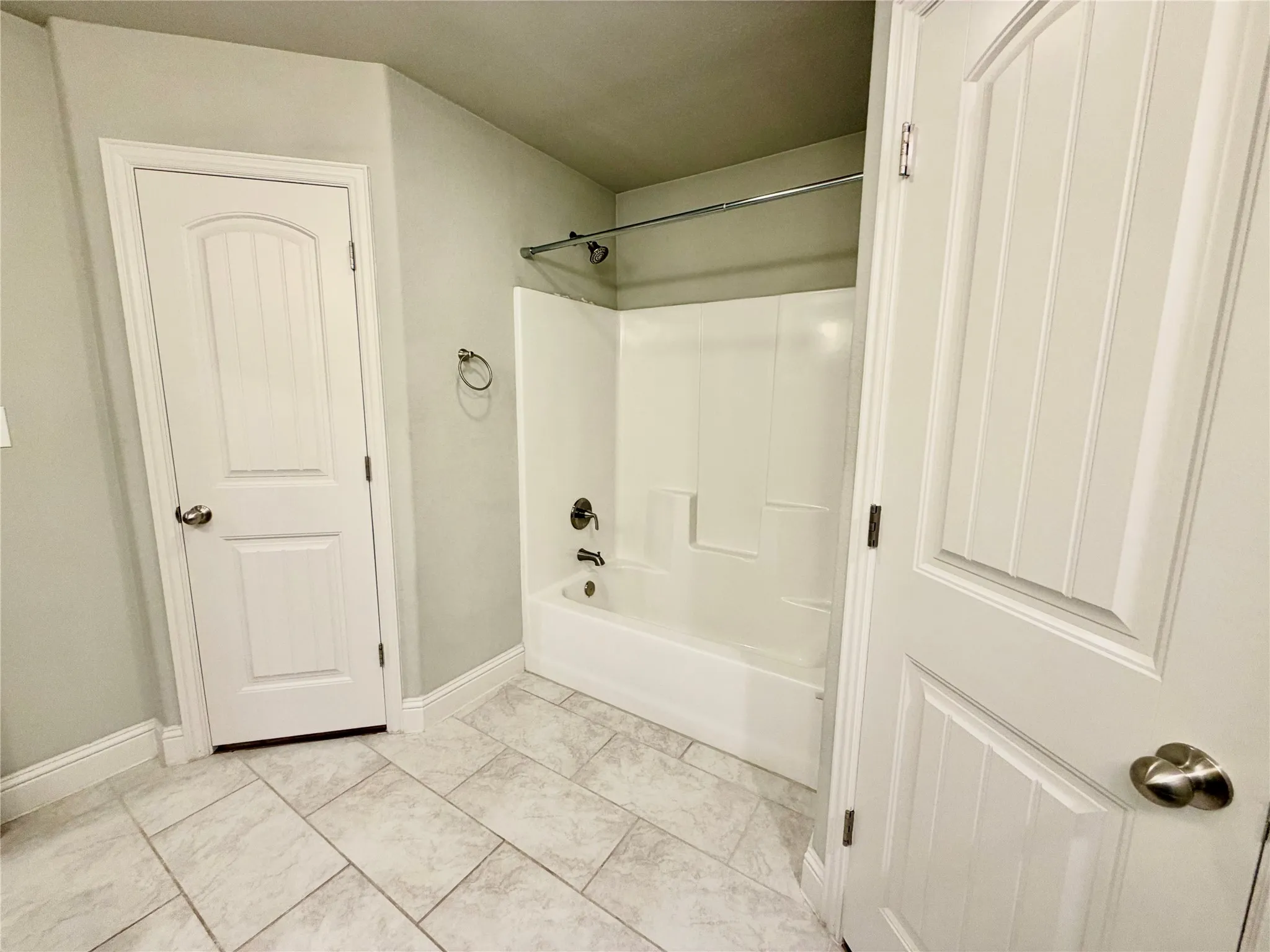 White paneled doors, light-toned tiled flooring, a white tub and shower combination, and light gray walls