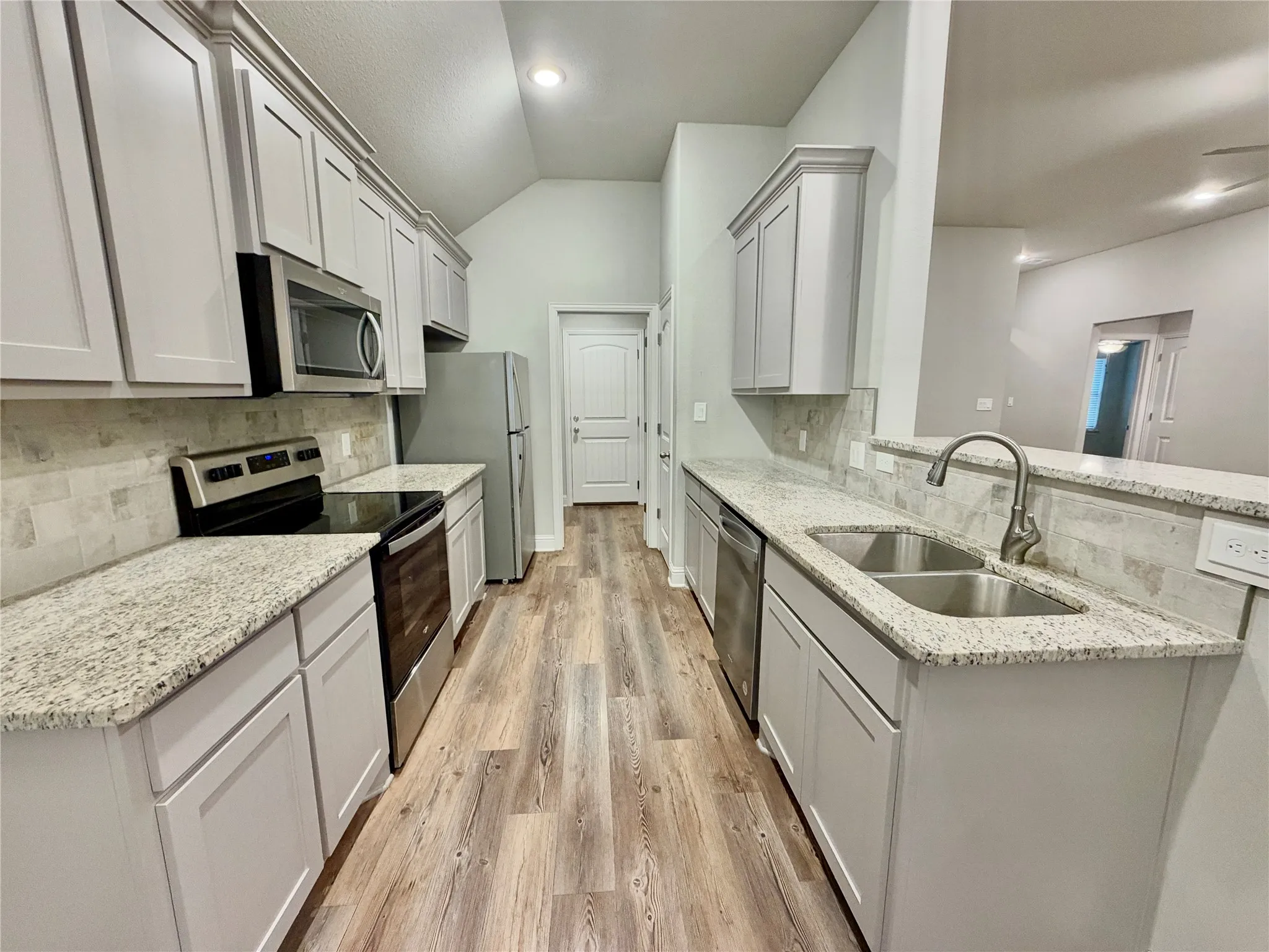 Kitchen featuring granite countertops, wood-finish flooring, stainless steel appliances, a double basin sink, and light-toned cabinetry