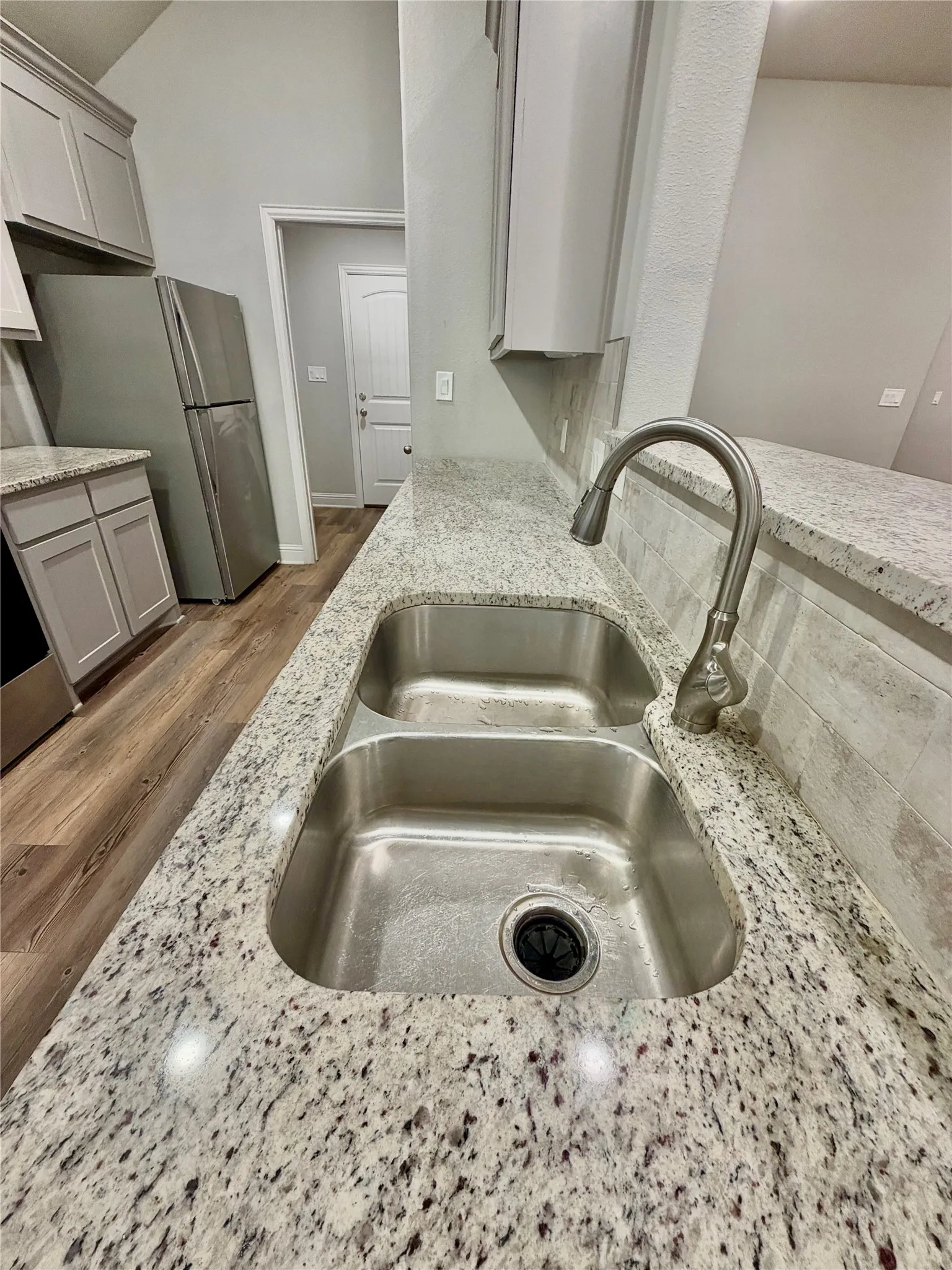Kitchen featuring light-toned cabinetry, wood-finish flooring, a double basin stainless steel sink, a stainless steel faucet, and speckled countertops