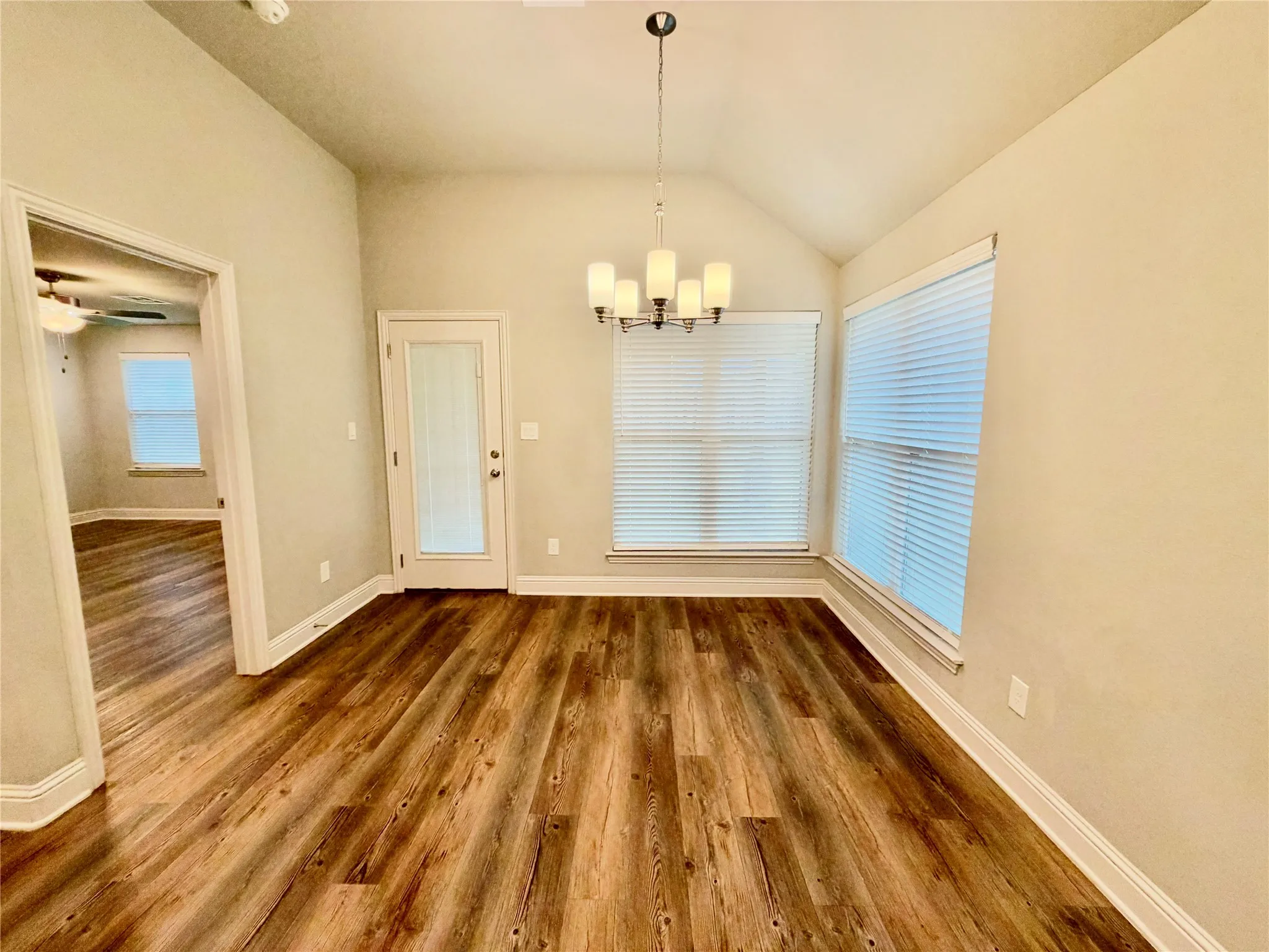 Vaulted ceiling with an attached chandelier, wood-finish flooring, and multiple windows with blinds