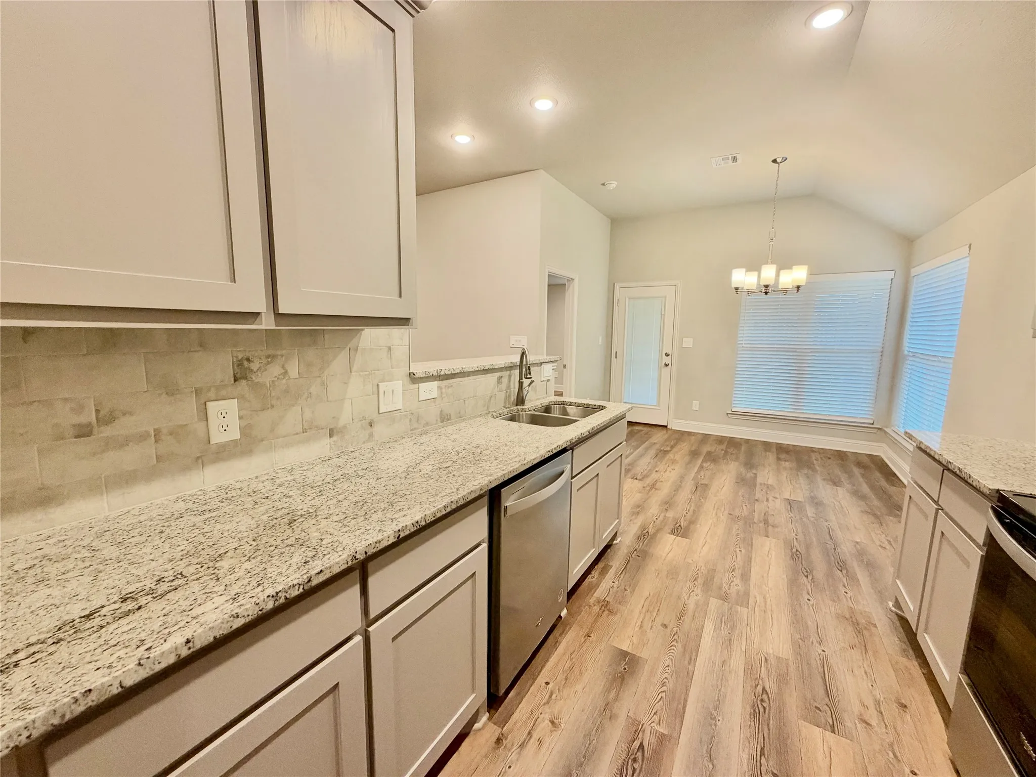 Kitchen featuring light-toned cabinetry, light granite-style countertops, subway tile backsplash, and stainless steel appliances