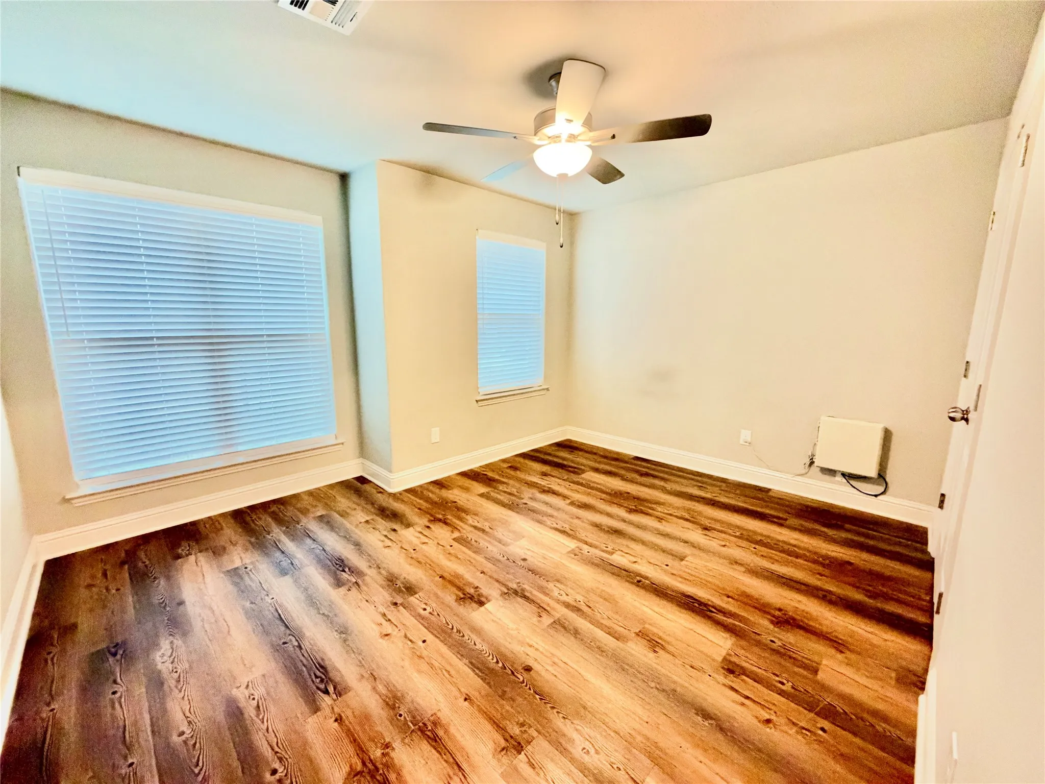 Wood-finish flooring, ceiling fan with integrated lighting, multiple windows, and neutral wall tones