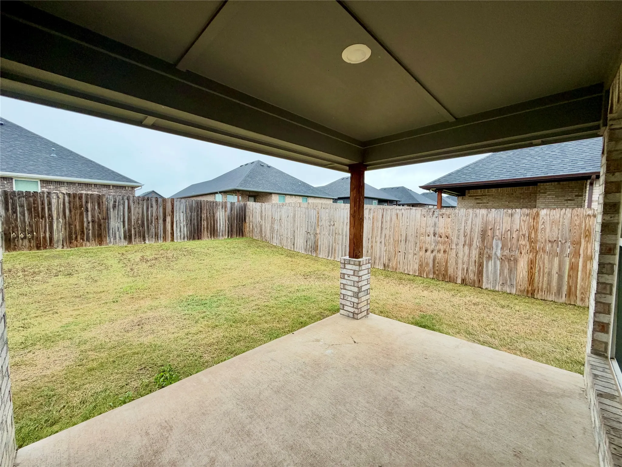 Covered patio with a concrete surface, supported by a wood beam with a brick base