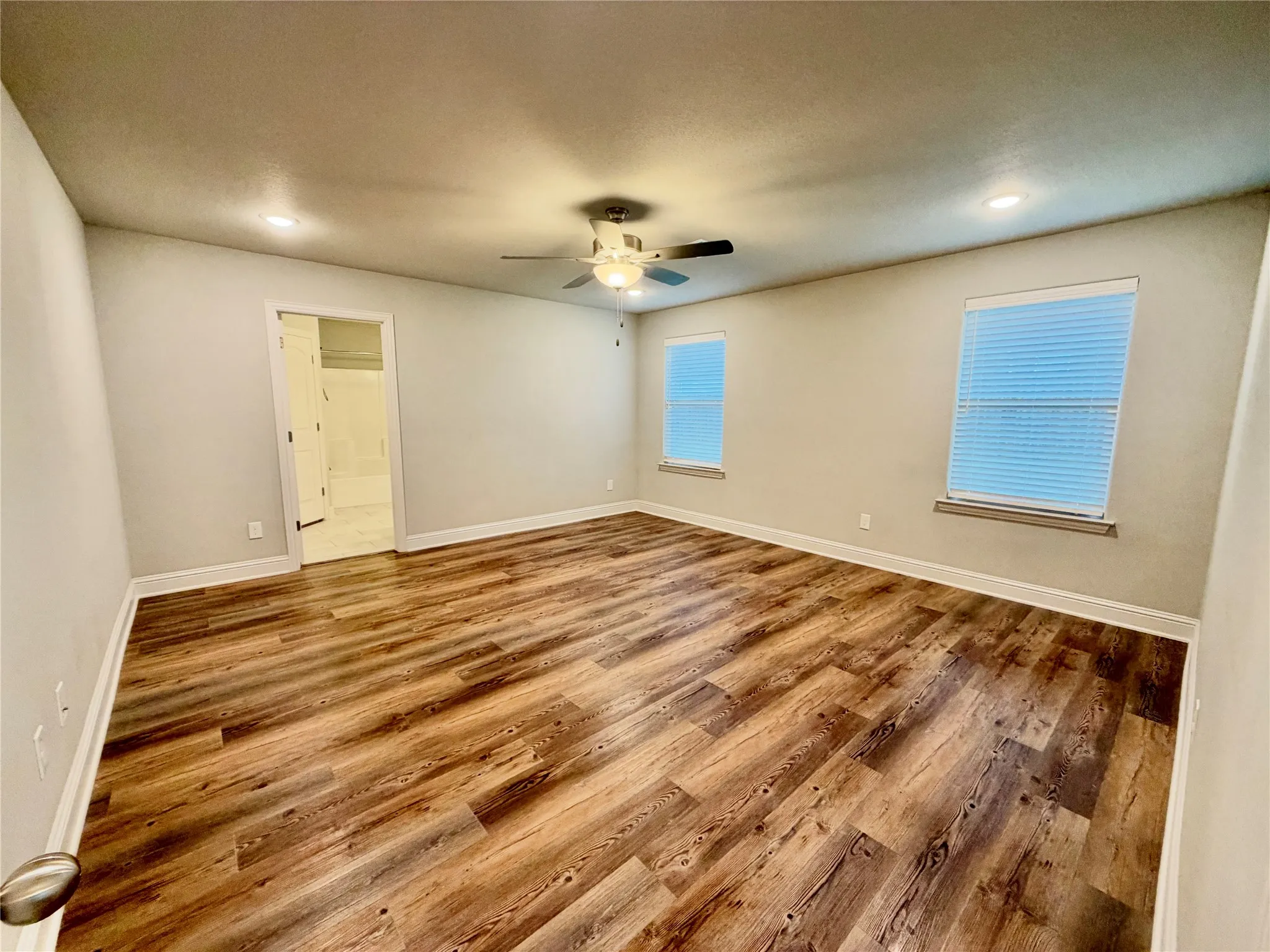 Spacious room featuring wood-finish flooring, two windows with blinds, a ceiling fan, and recessed lighting