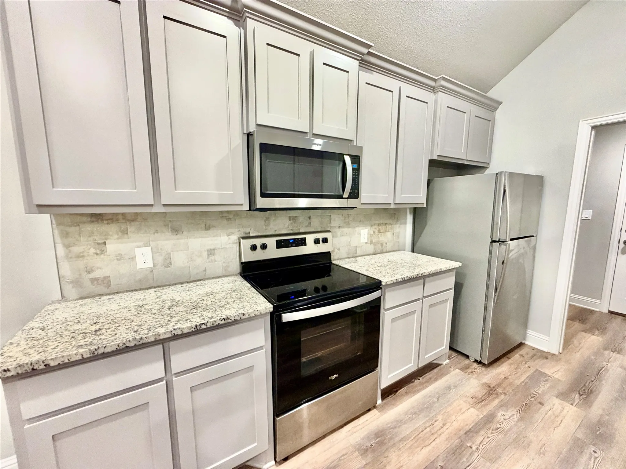 Kitchen featuring stainless steel appliances, light gray cabinetry with crown molding, light-toned granite countertops, and a tiled backsplash