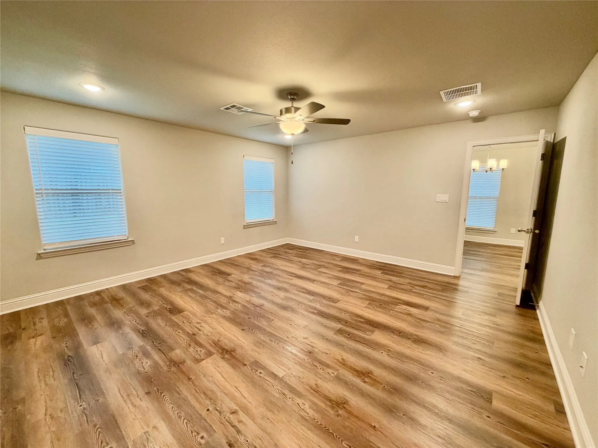 Wood-finish flooring, recessed lighting, ceiling fan with light, two windows with blinds, and white trim molding