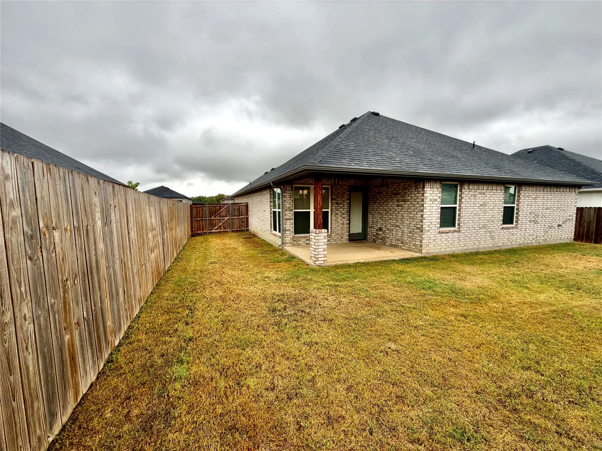 Brick exterior with a dark shingle roof, featuring a covered patio, privacy fencing, and an access gate