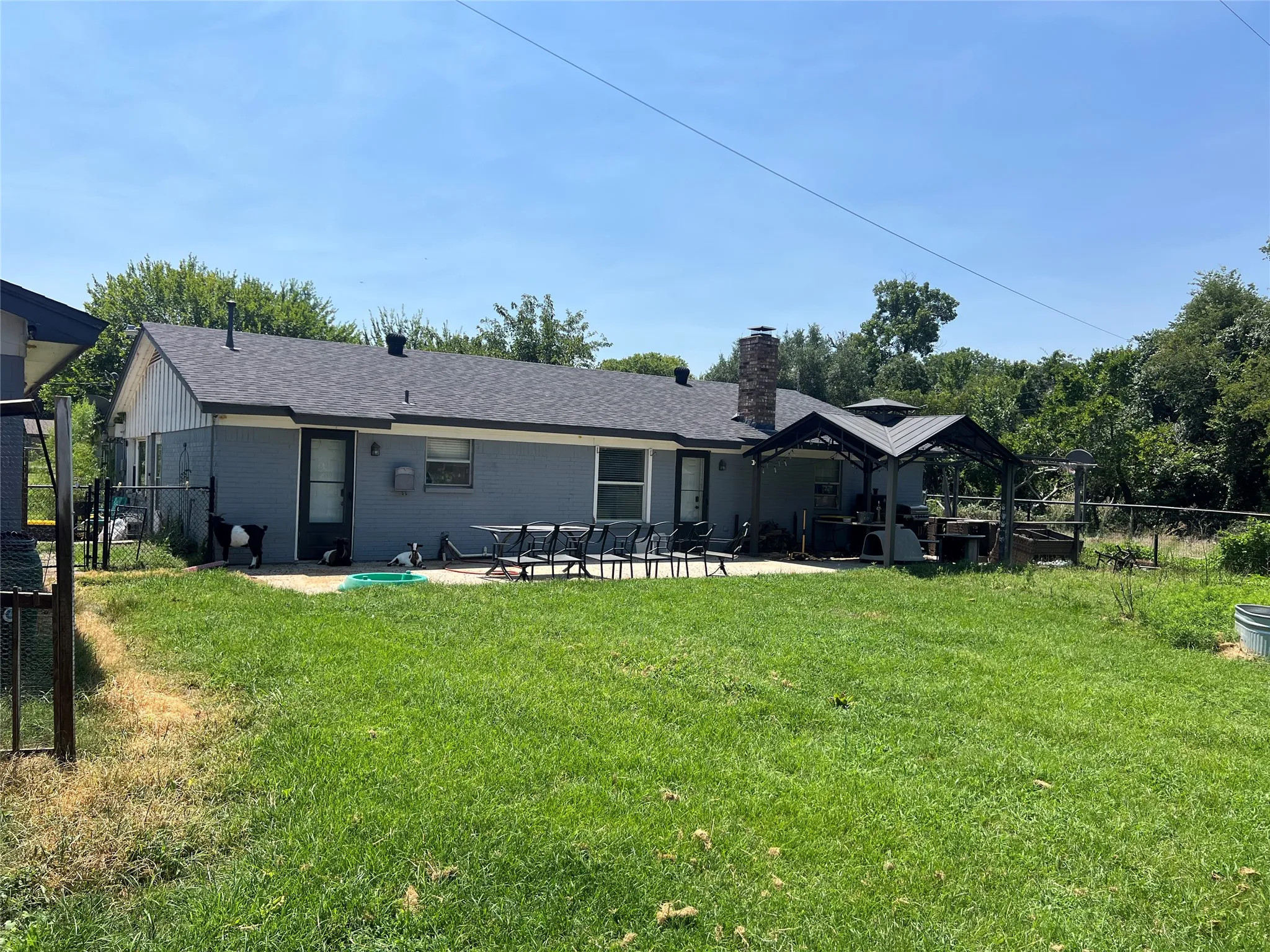 Expansive rear yard with a paved patio, a covered gazebo, and a stone chimney