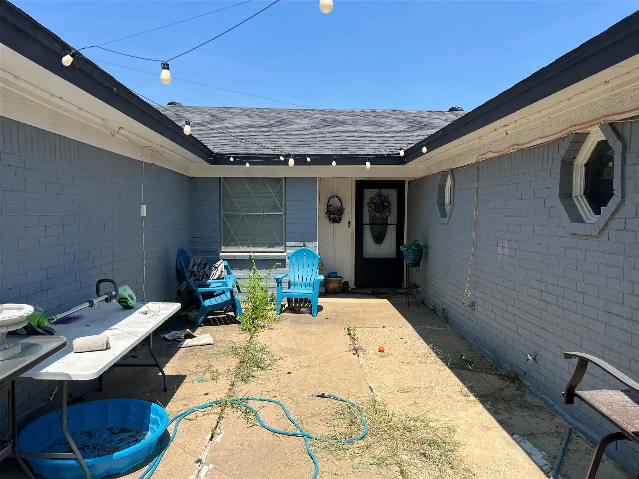 Concrete patio with painted brick exterior, a dark shingle roof, and octagonal window features
