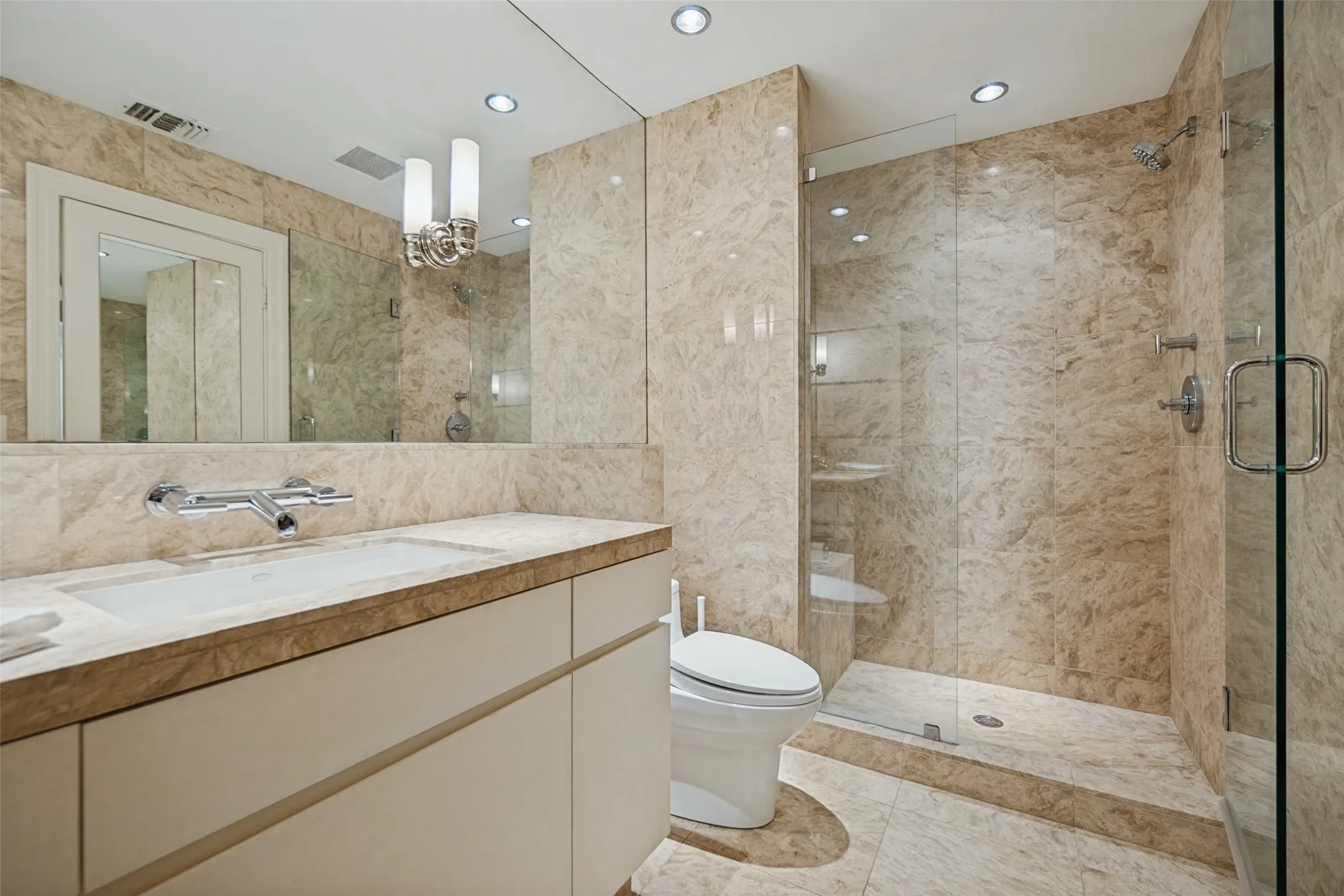 Bathroom featuring extensive stone tile, frameless glass shower enclosure, recessed lighting, and a vanity with an integrated sink