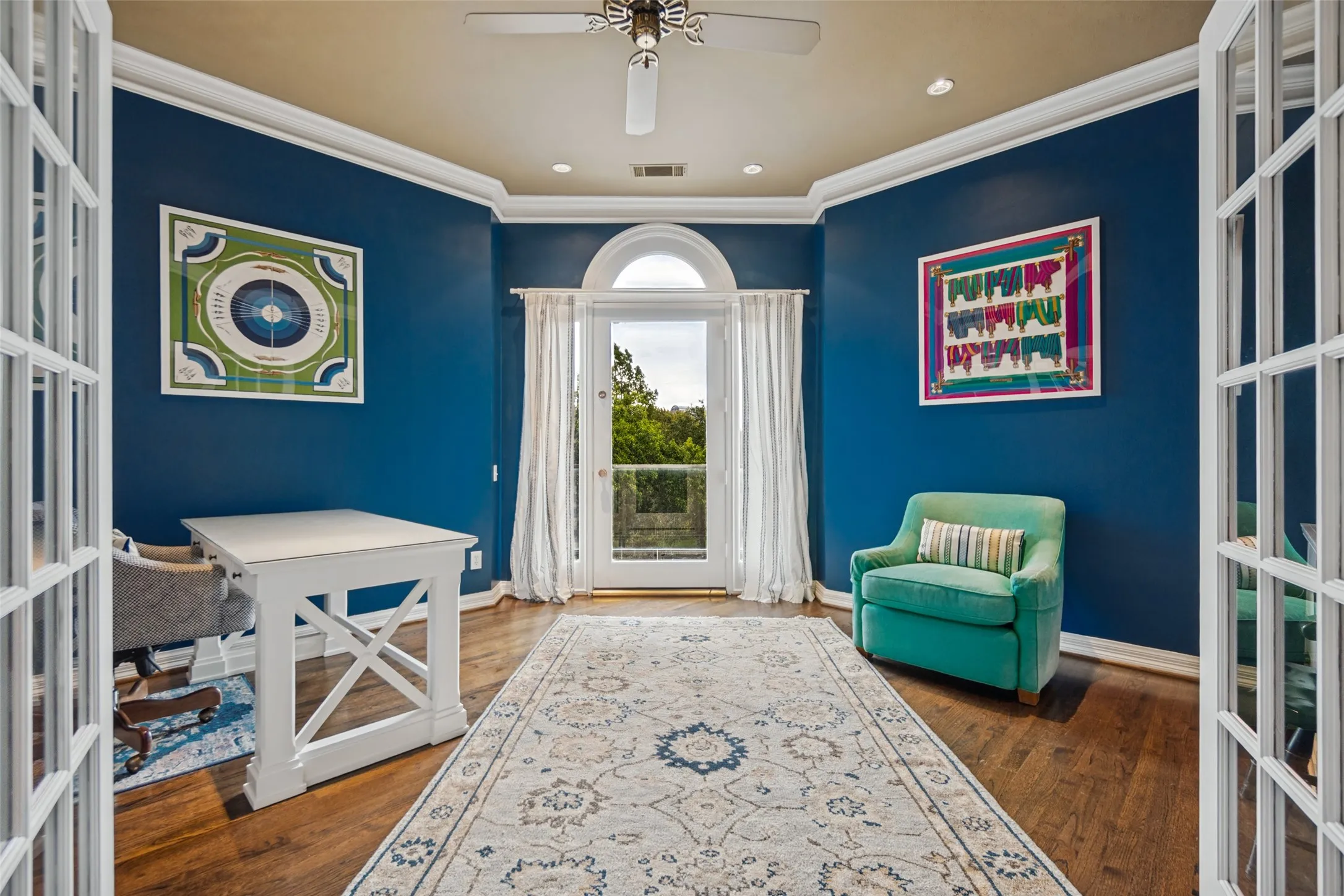 Hardwood flooring, arched glass-paned door, crown molding, ceiling fan with light fixture, double French doors, and balcony overlooking a greenbelt