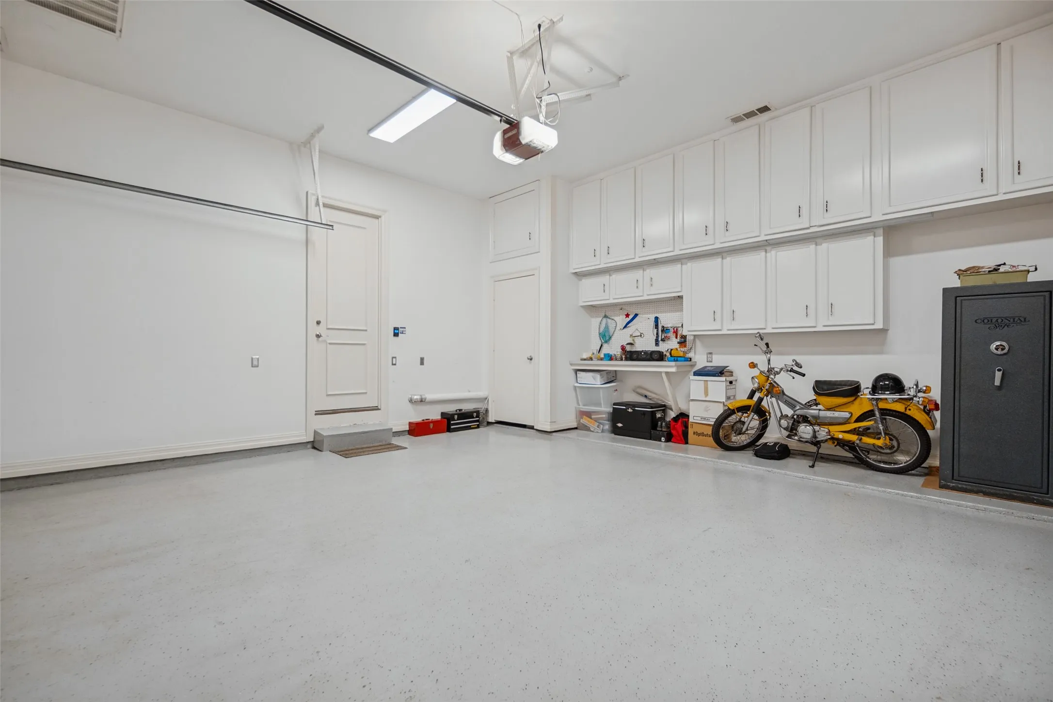 Garage with a light-colored epoxy flooring, extensive built-in white cabinetry, a built-in workbench, and overhead fluorescent lighting
