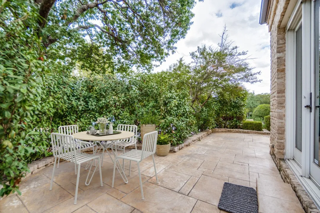 Stone patio with direct outdoor access from primary bedroom, bordered by a low stone wall and mature landscaping (this is a virtually staged photo)