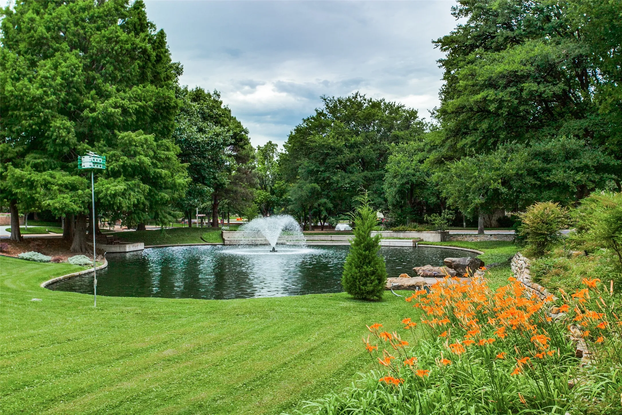 Landscaped pond with an active fountain, surrounded by mature trees and vibrant foliage