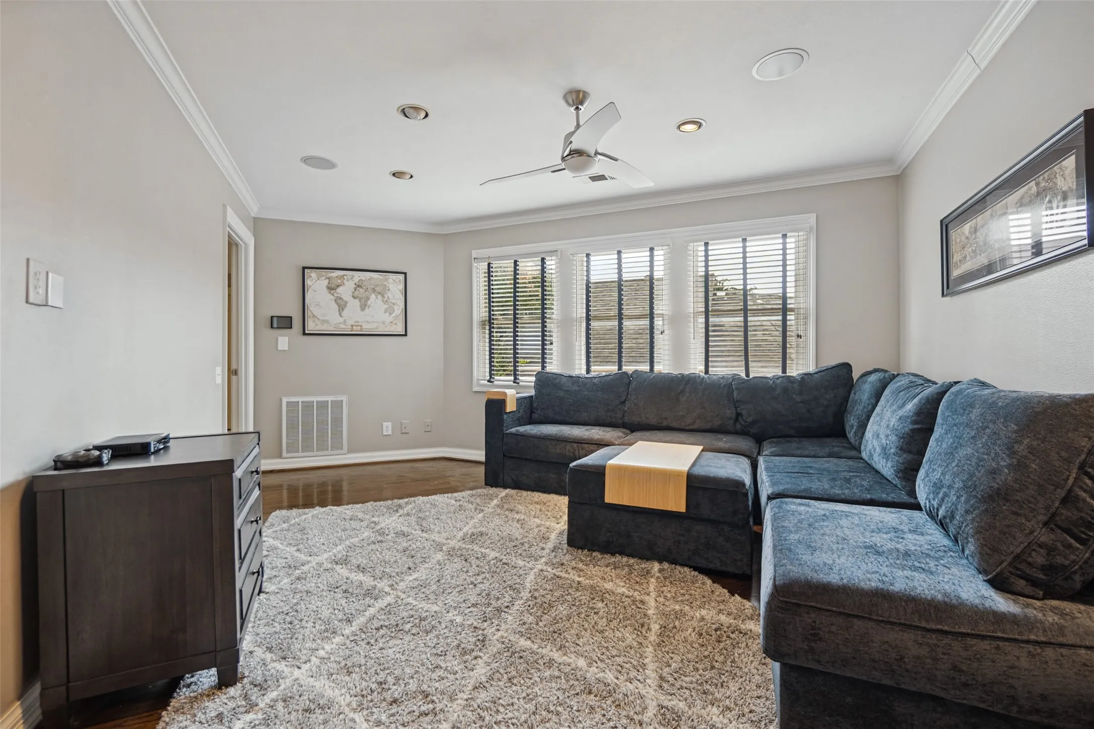 Wood-finish flooring, crown molding, multiple recessed lights, ceiling fan, and window blinds