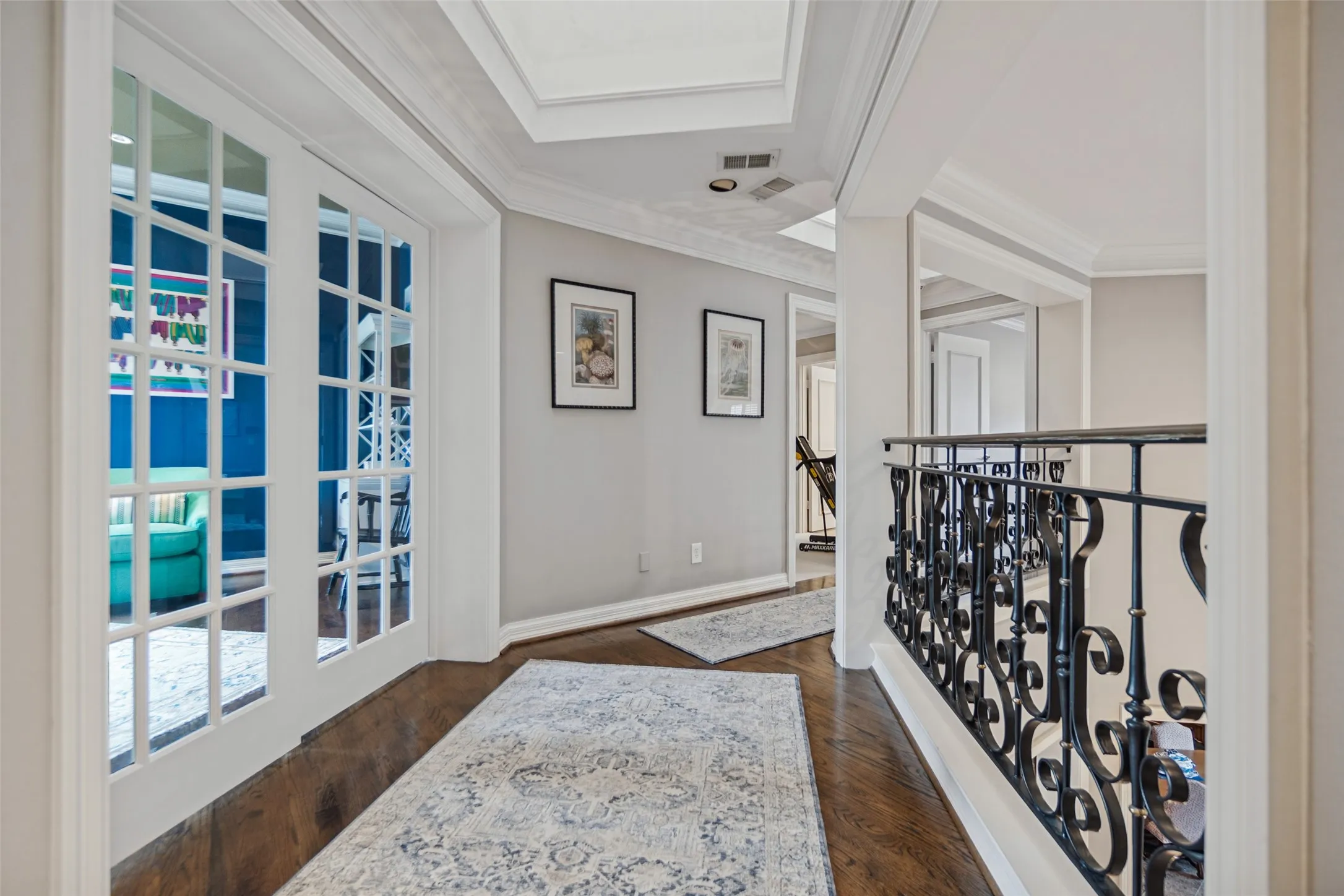 Hardwood flooring, coffered ceiling, elegant crown molding, wrought iron railing, and white French doors