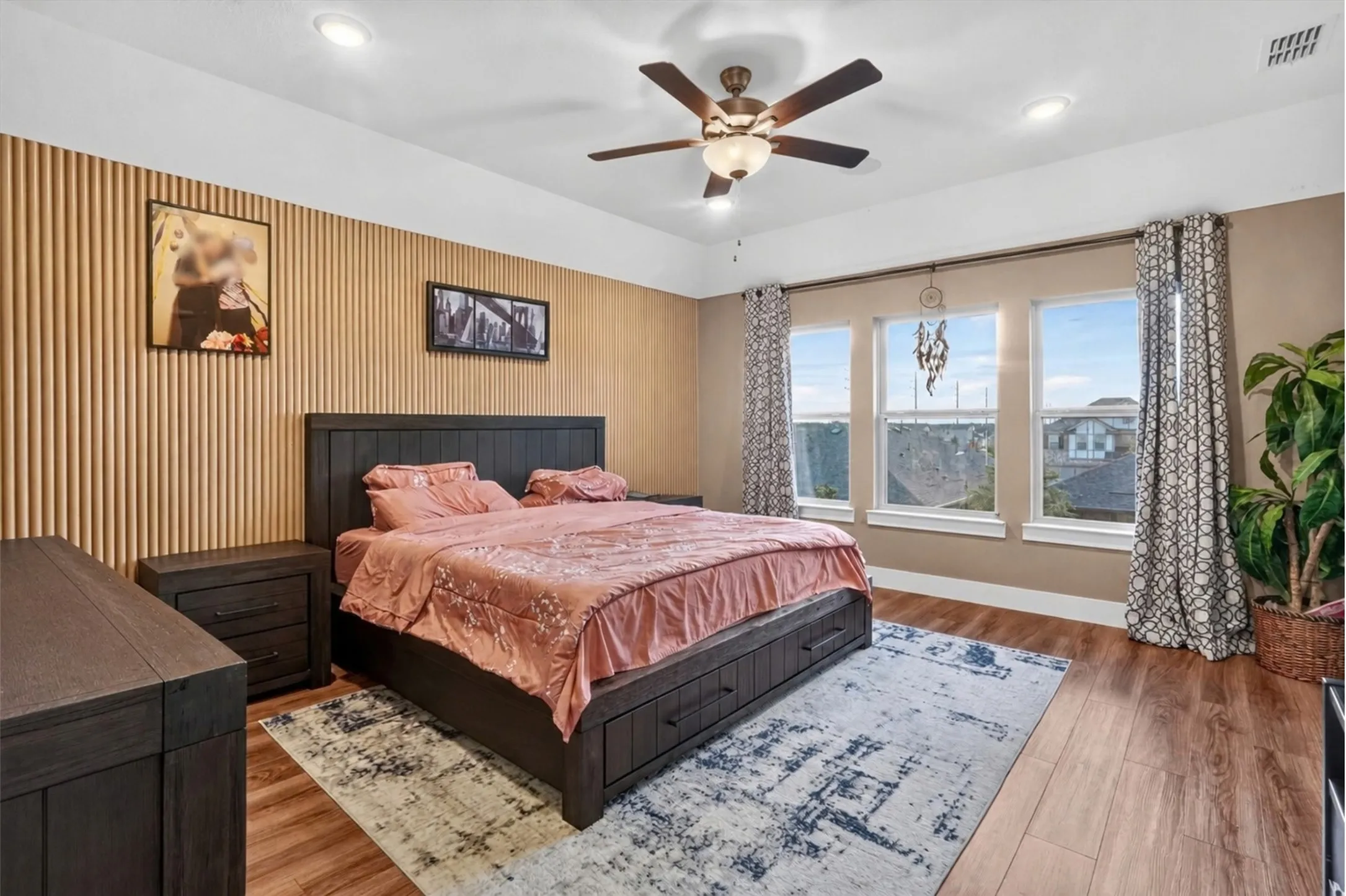 Wood-finish flooring, accent wall with vertical paneling, recessed lighting, ceiling fan with integrated lighting, and three tall windows