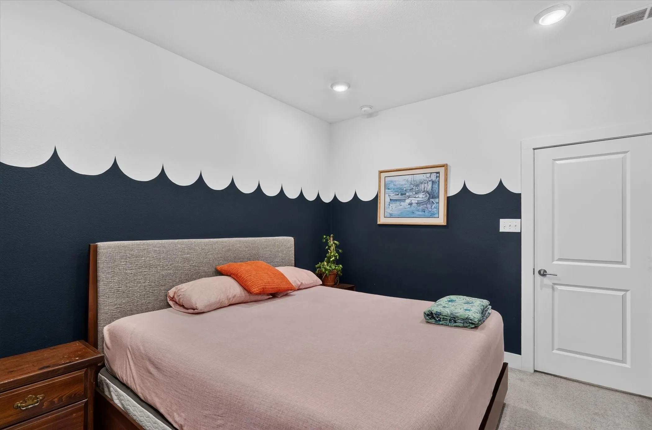 Recessed lighting illuminates the space, featuring a neutral upholstered headboard and a paneled interior door